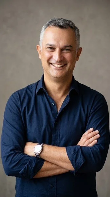 Andrew Price Family Lawyer smiling, dressed in a dark blue button-down shirt, standing with arms crossed against a plain, neutral background.