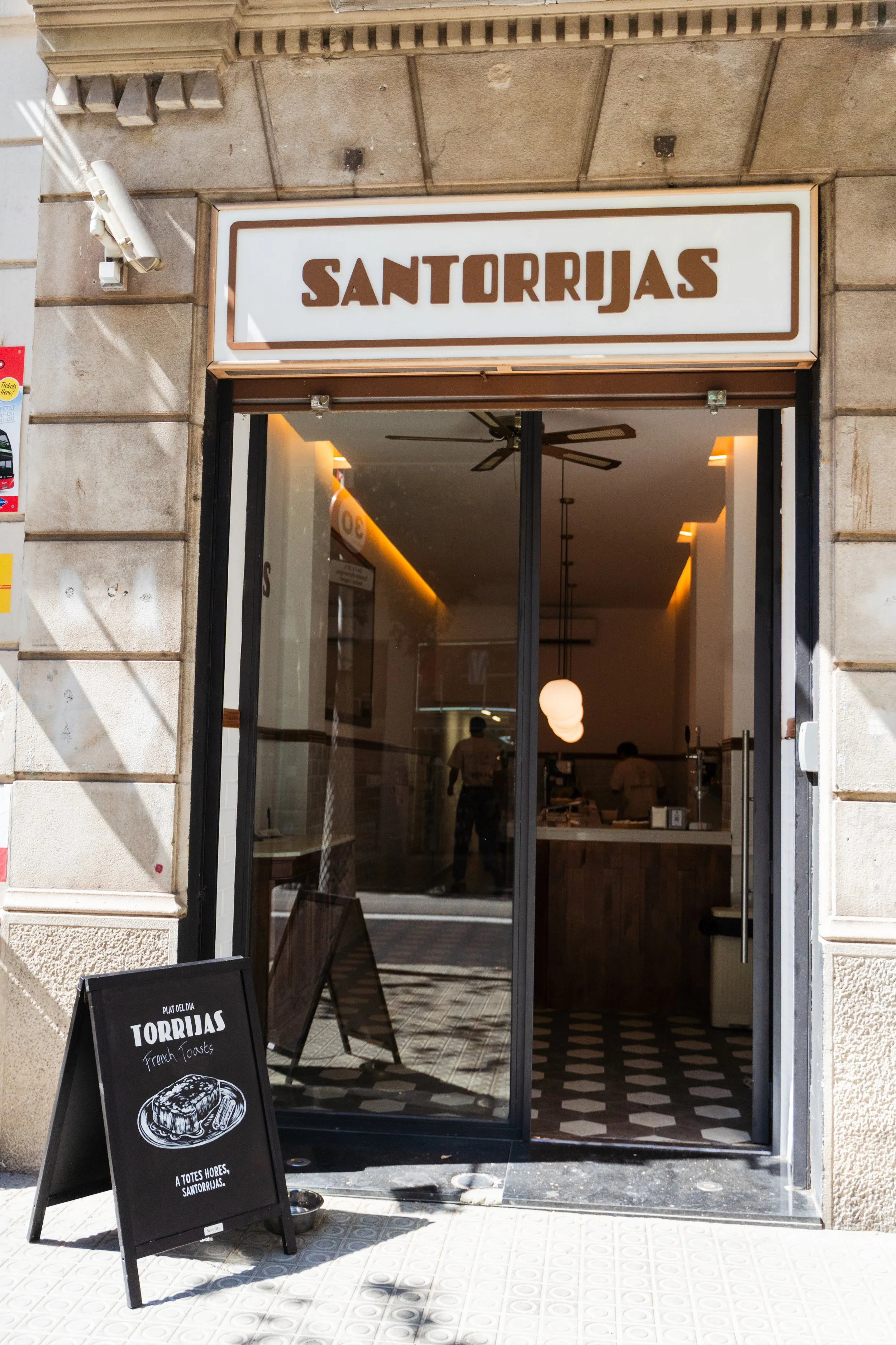 Fachada de un restaurante llamado 'Santorrjas' con un cartel promocional que dice 'Plato del día Torrijas' y una vista del interior con mesas y personal atendiendo.