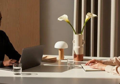 Two people working at a table with a laptop, glasses of water, and decorative vases with calla lilies.