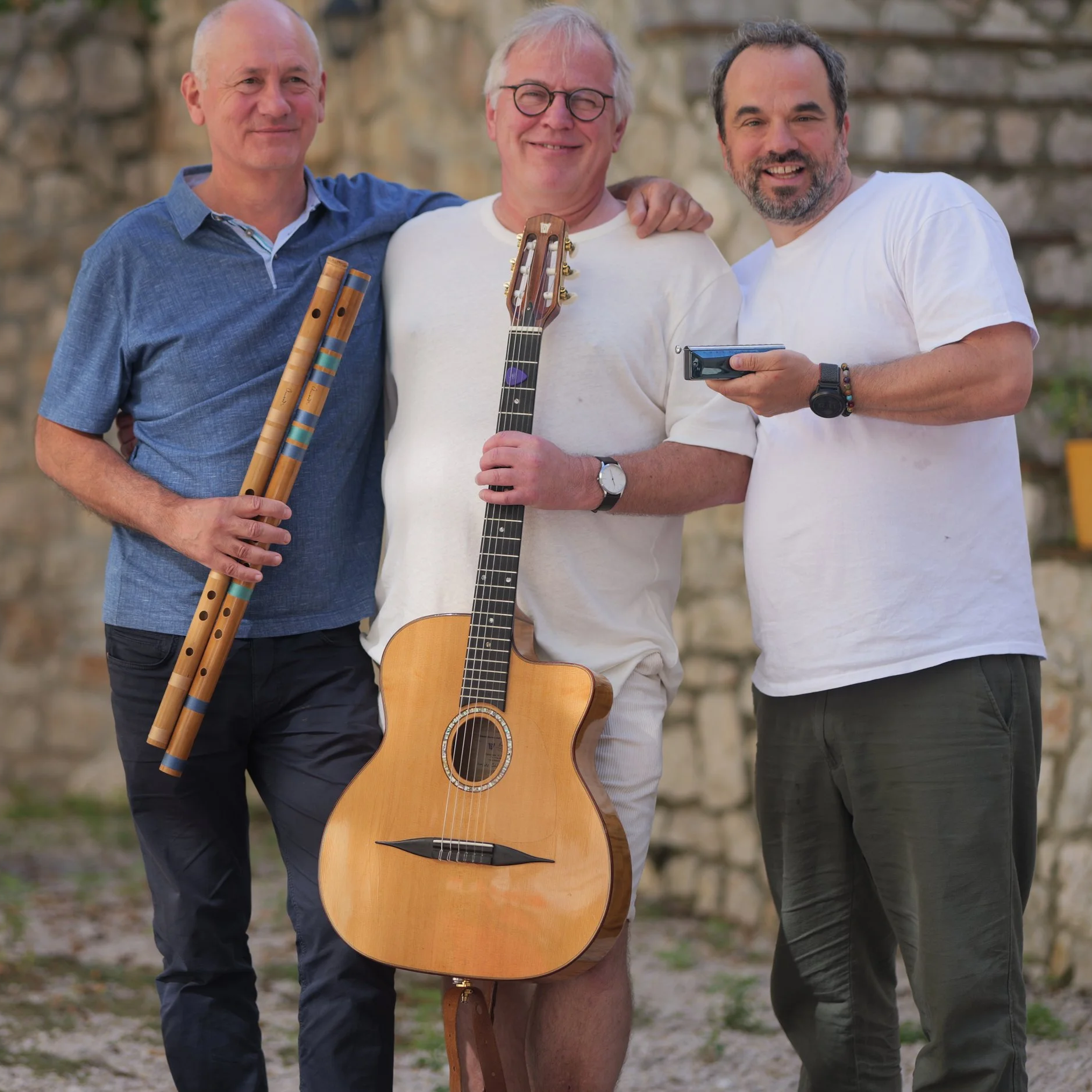 Trio Tihai lacht mit Bansuri-Flöten und Gitarre vor einer alten Steinmauer