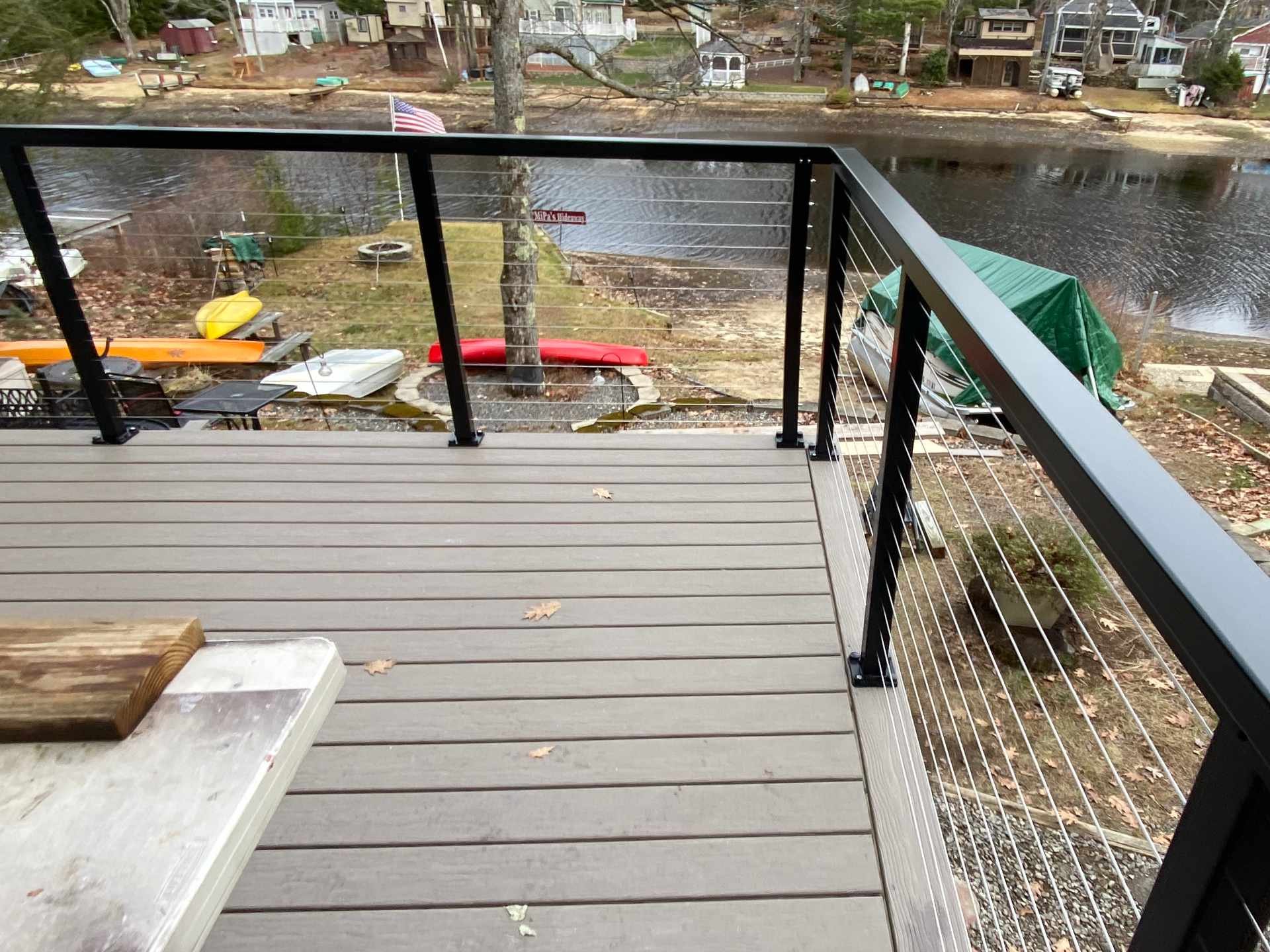 A view of a backyard with a body of water, several small boats, and a few trees from a balcony with a stainless steel cable railing with aluminum posts and top rails, and composite deck.