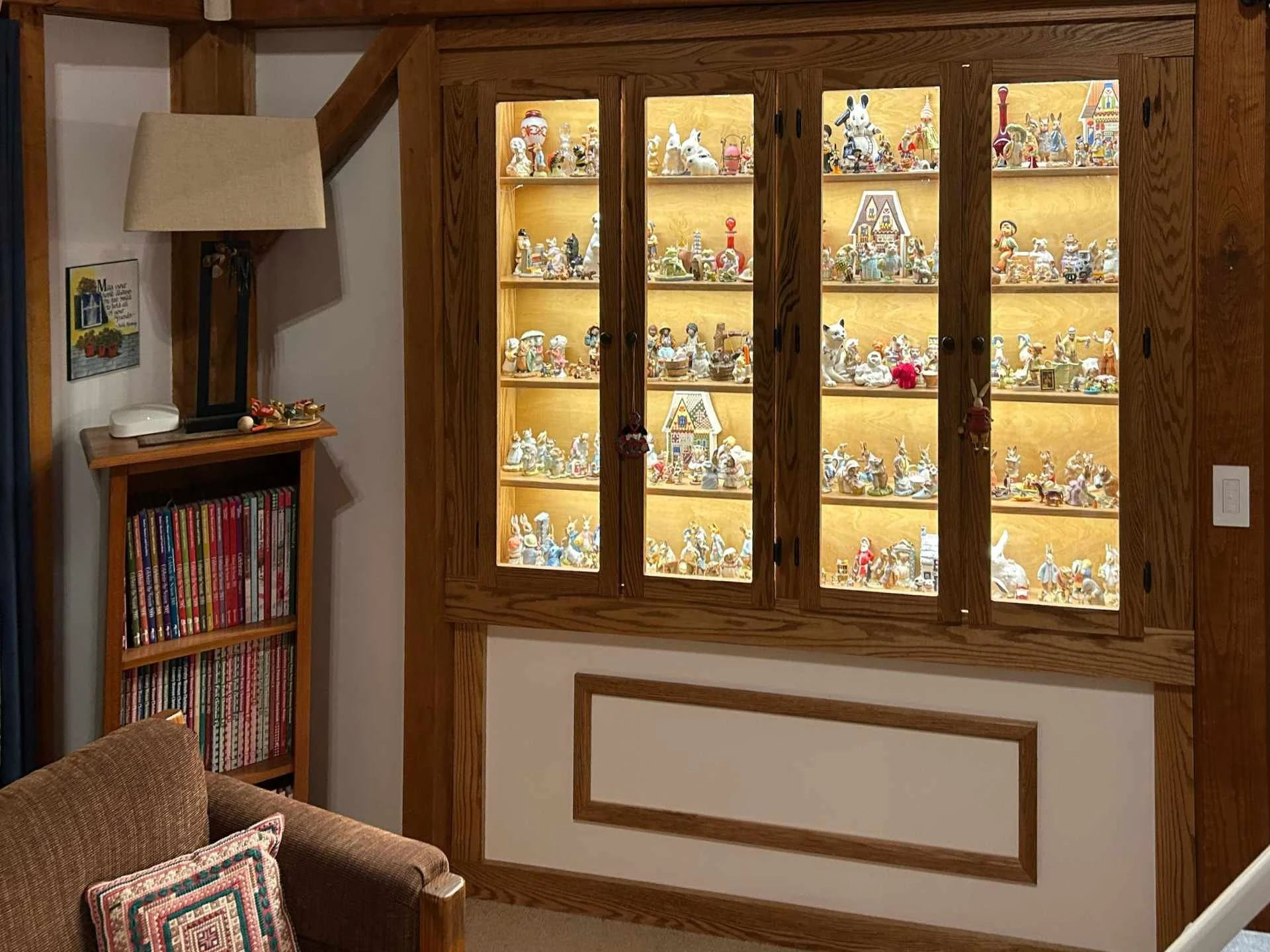A custom-built oak wooden display cabinet with glass doors filled with various figurines and collectibles. To the left, a small bookshelf with magazines.