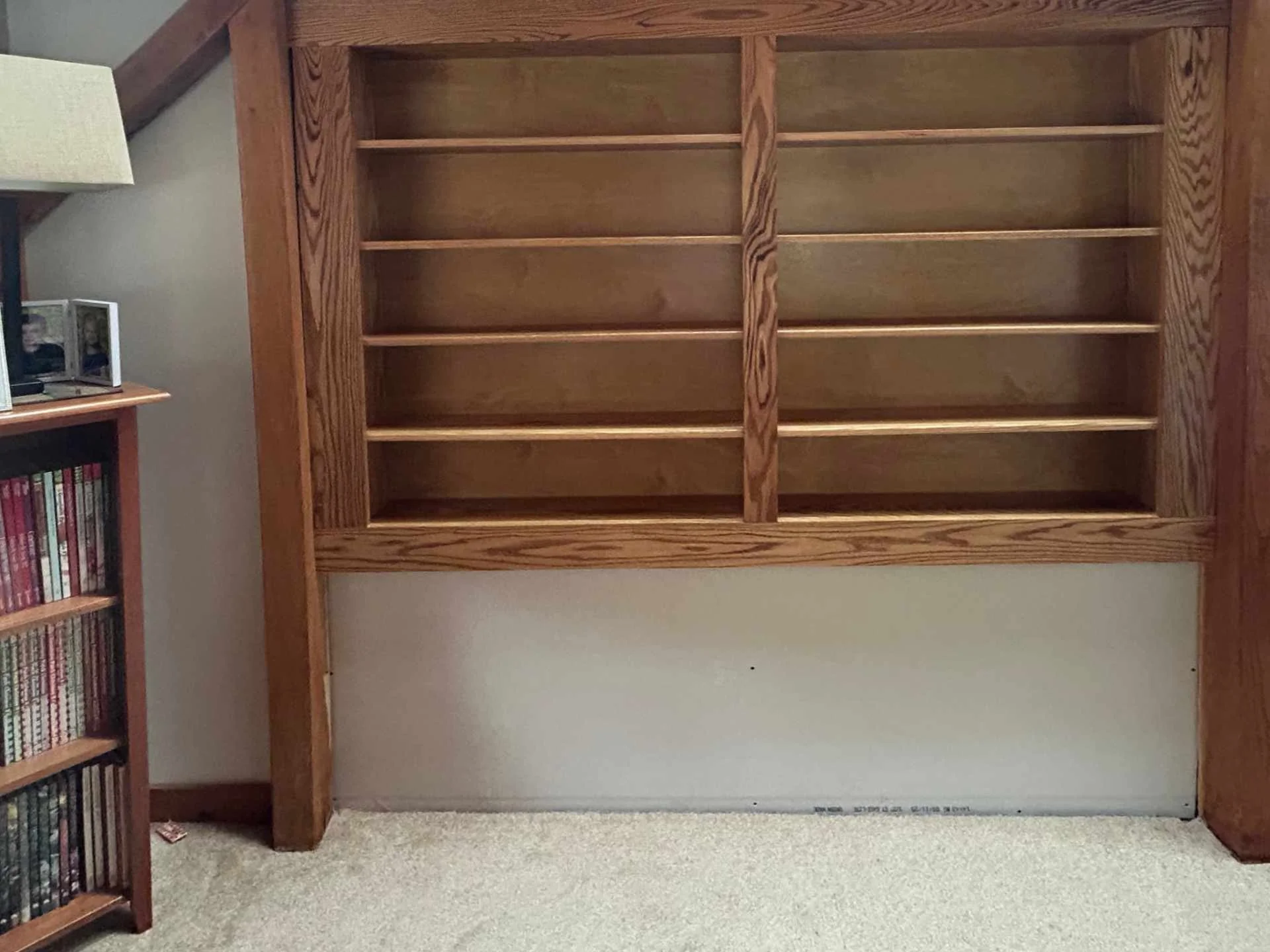 Empty custom oak wooden bookshelf under construction with four shelves against a wall in a room.