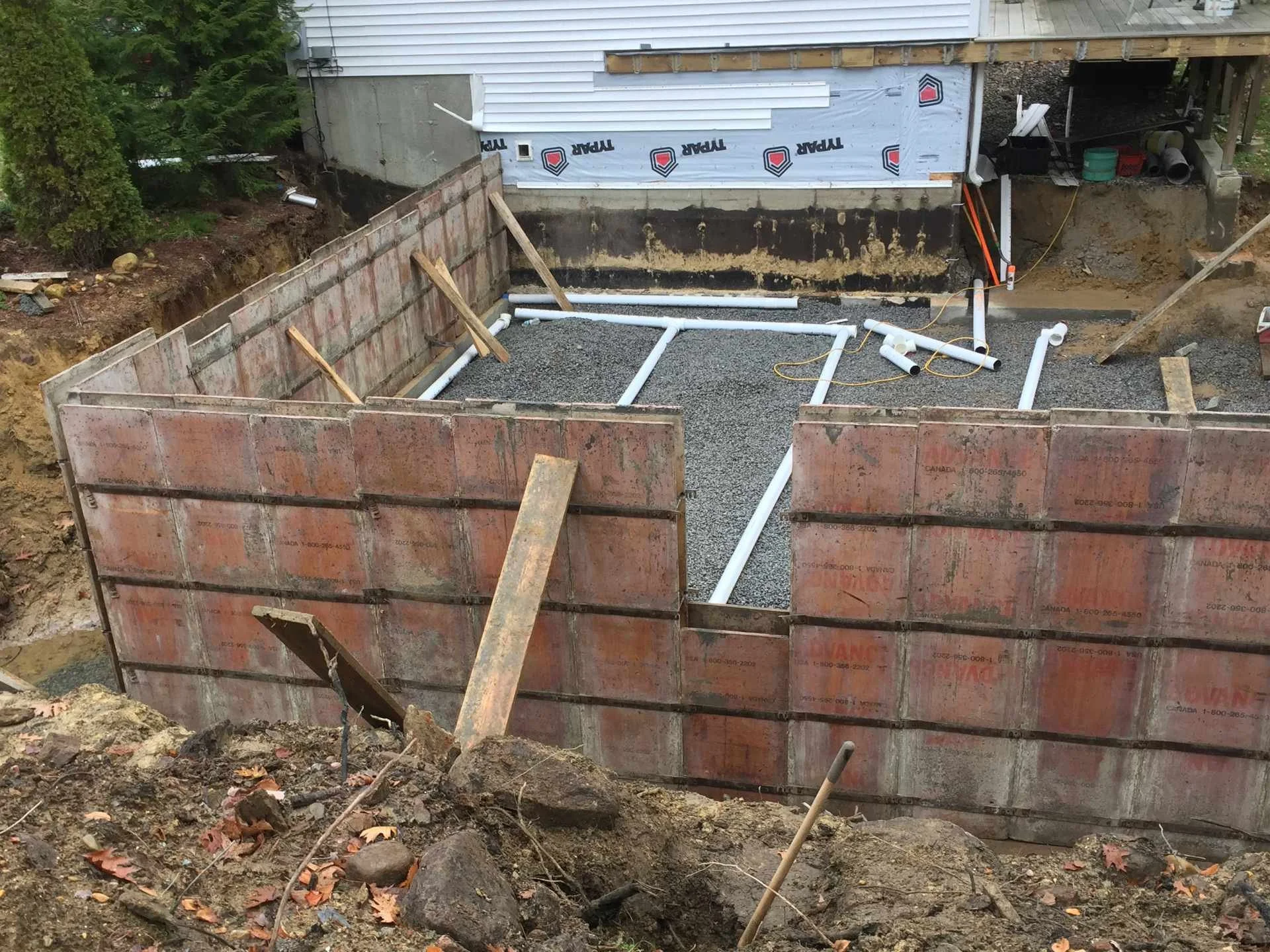 Construction site of a house foundation showing excavation work with pipes installed, surrounded by dirt and construction barriers.