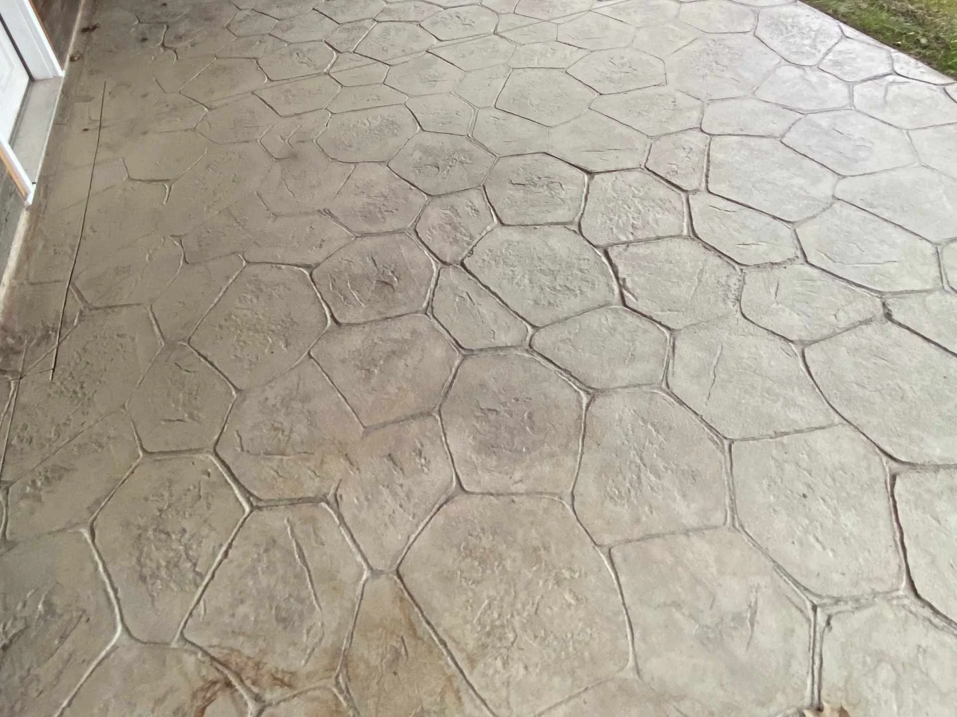 Concrete patio with decorative stamped pattern that resembles large honeycomb or hexagonal shapes, leading to a grassy area on the right side.
