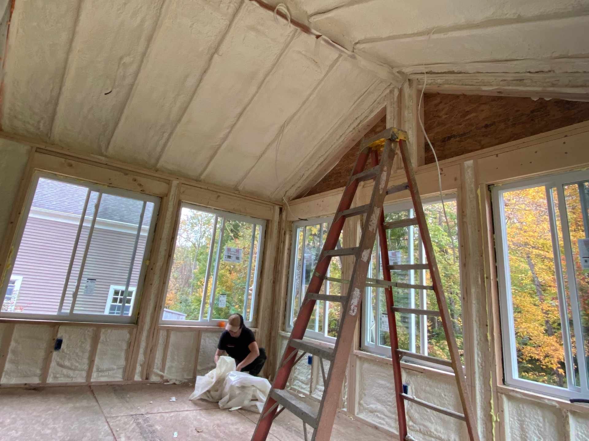 Interior view of a room under construction with windows, insulation, scaffolding, and a person working with construction materials.