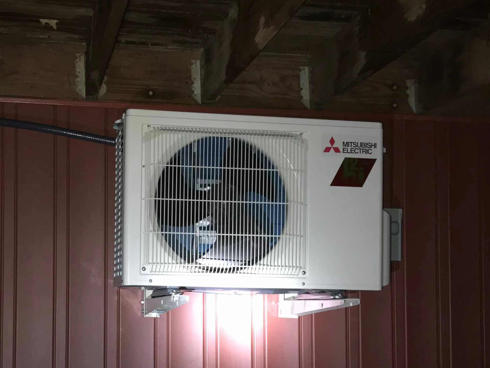 A Mitsubishi Electric air conditioning and heating unit mounted on a maroon wooden wall.