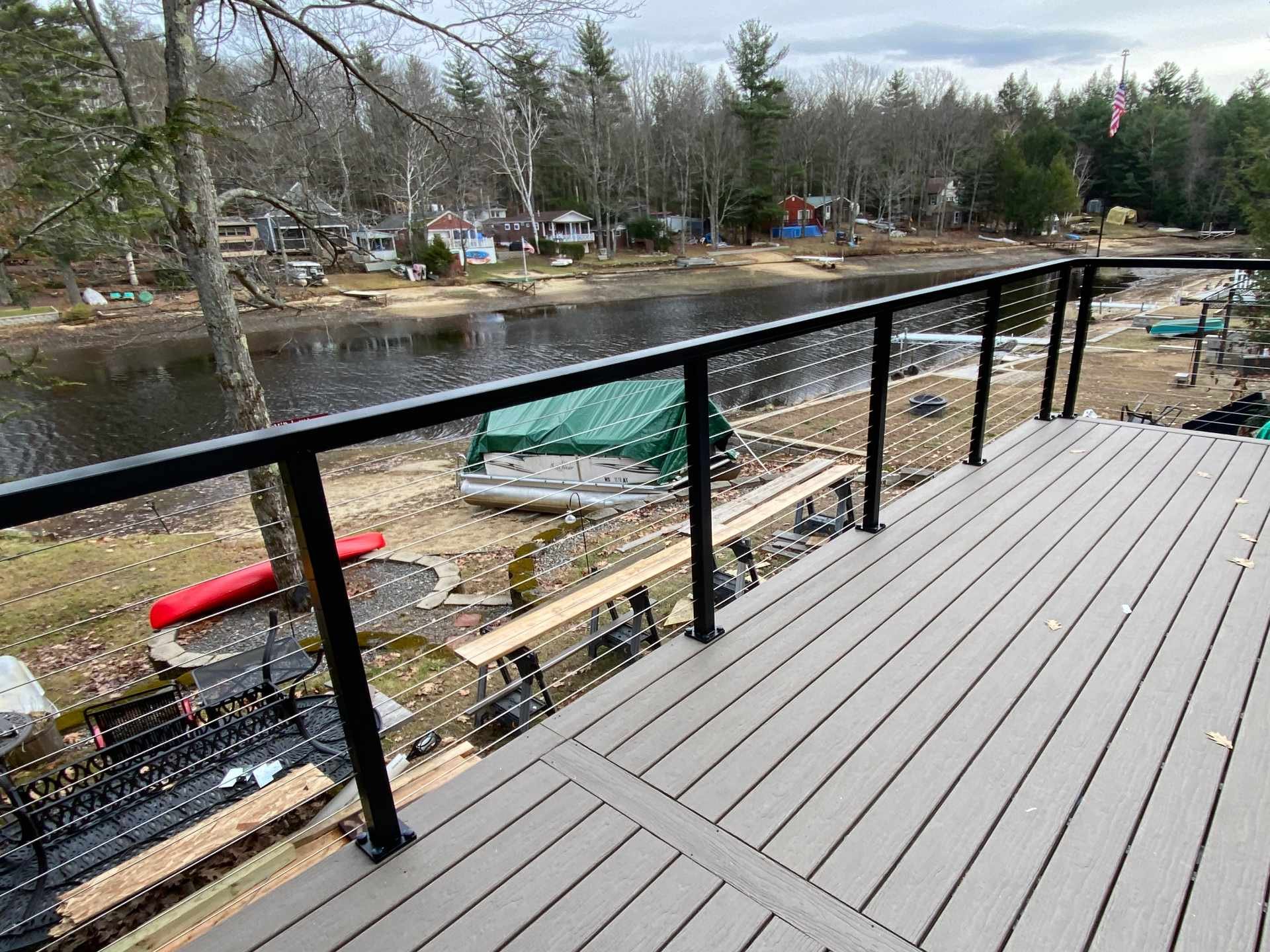 View from a balcony overlooking a lakeside neighborhood with partially built deck with composite non-slip decking and stainless steel cable railings with aluminum posts and top rails. In the foreground are boats along the shore.