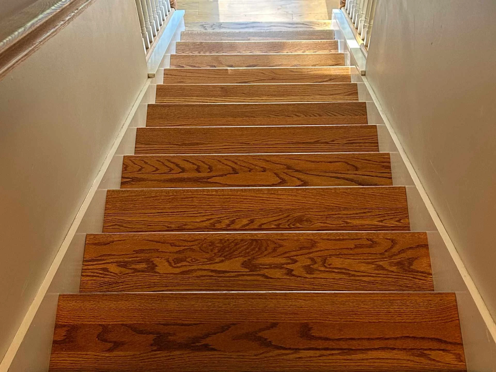 Wooden staircase with new oak treads beige walls and white trim, viewed from the top looking downward.