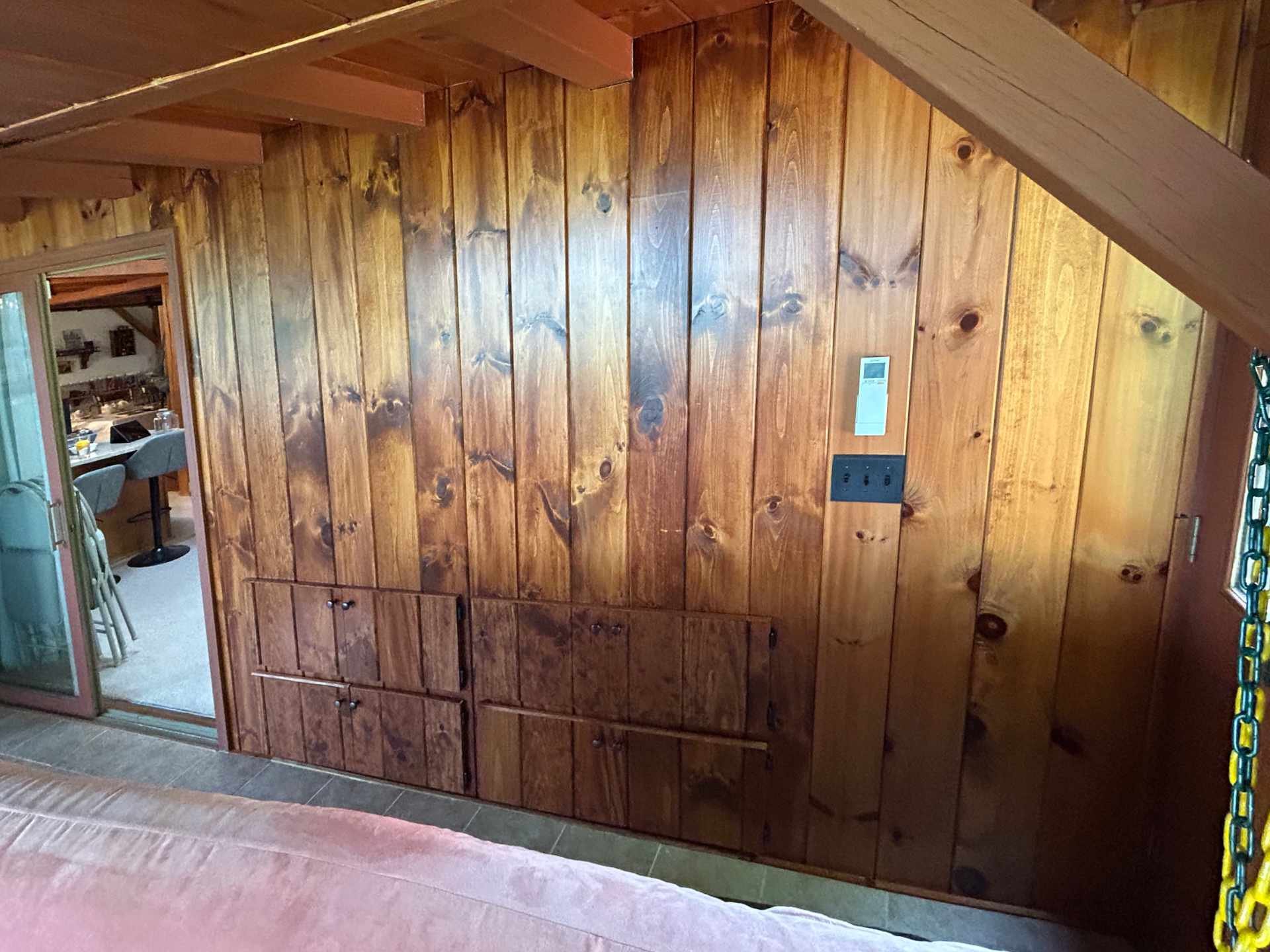 custom Wood-paneled wall with cabinet doors and electronic thermostat in a room, with a sliding glass door and dining area visible.