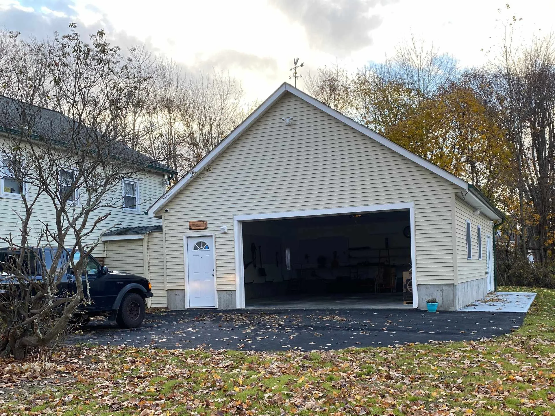 A view of a house with a new attached garage on a cloudy day during fall, with trees and leaves on the ground.