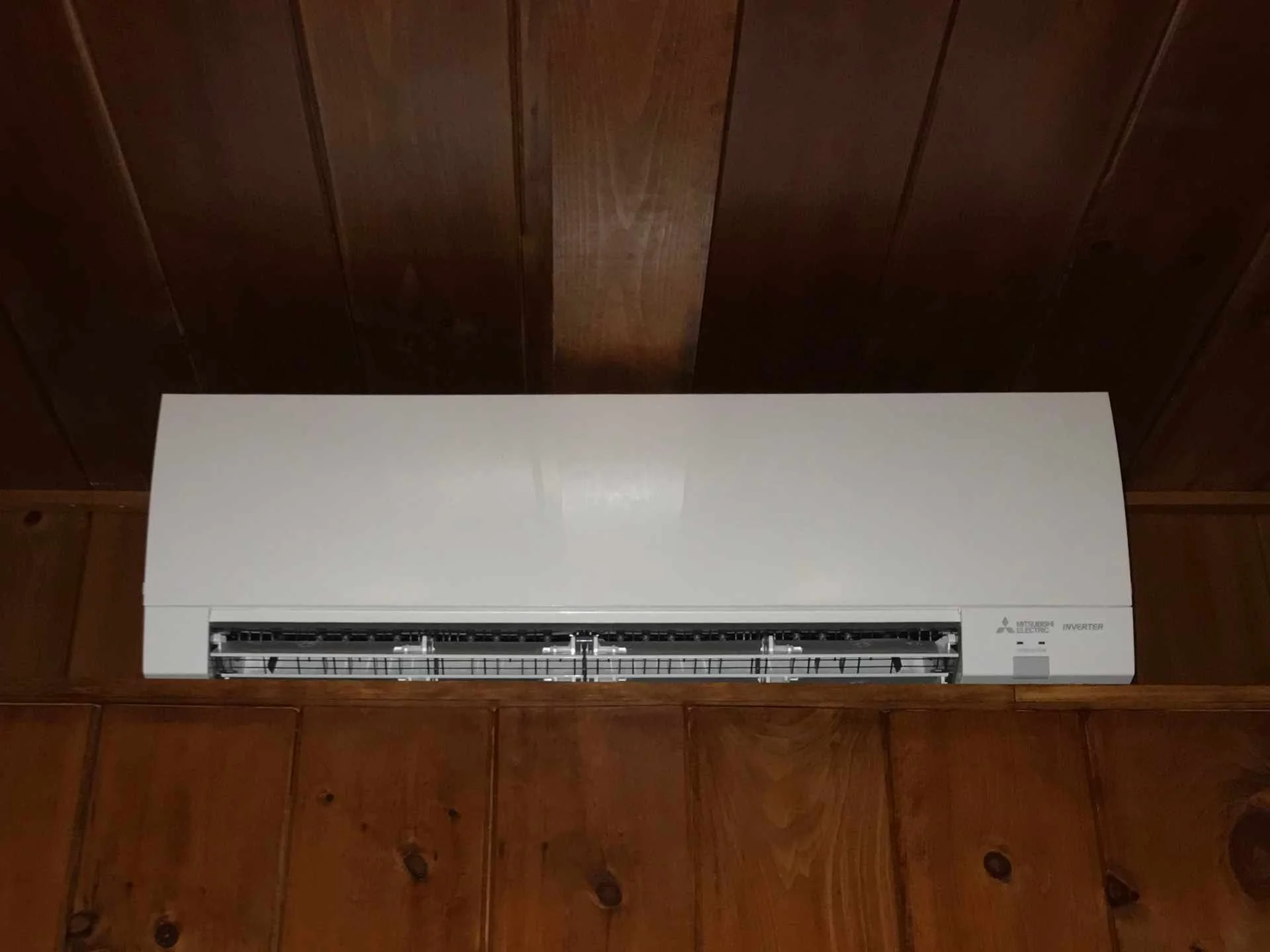 Wall-mounted Mitsubishi Electric inverter air conditioning and heating unit on brown wooden paneled wall.