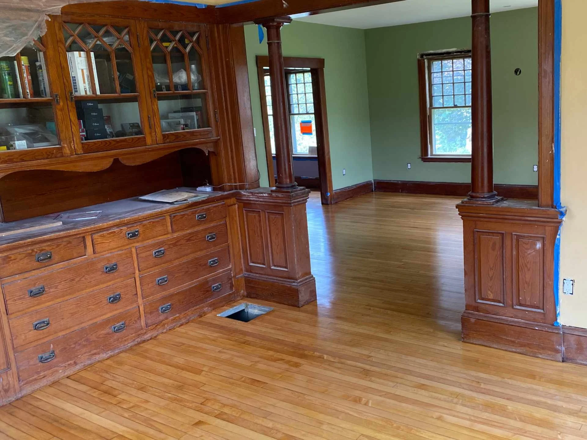Room with wooden built-in bookshelf, large wooden pillars, green walls, hardwood floor, and windows.