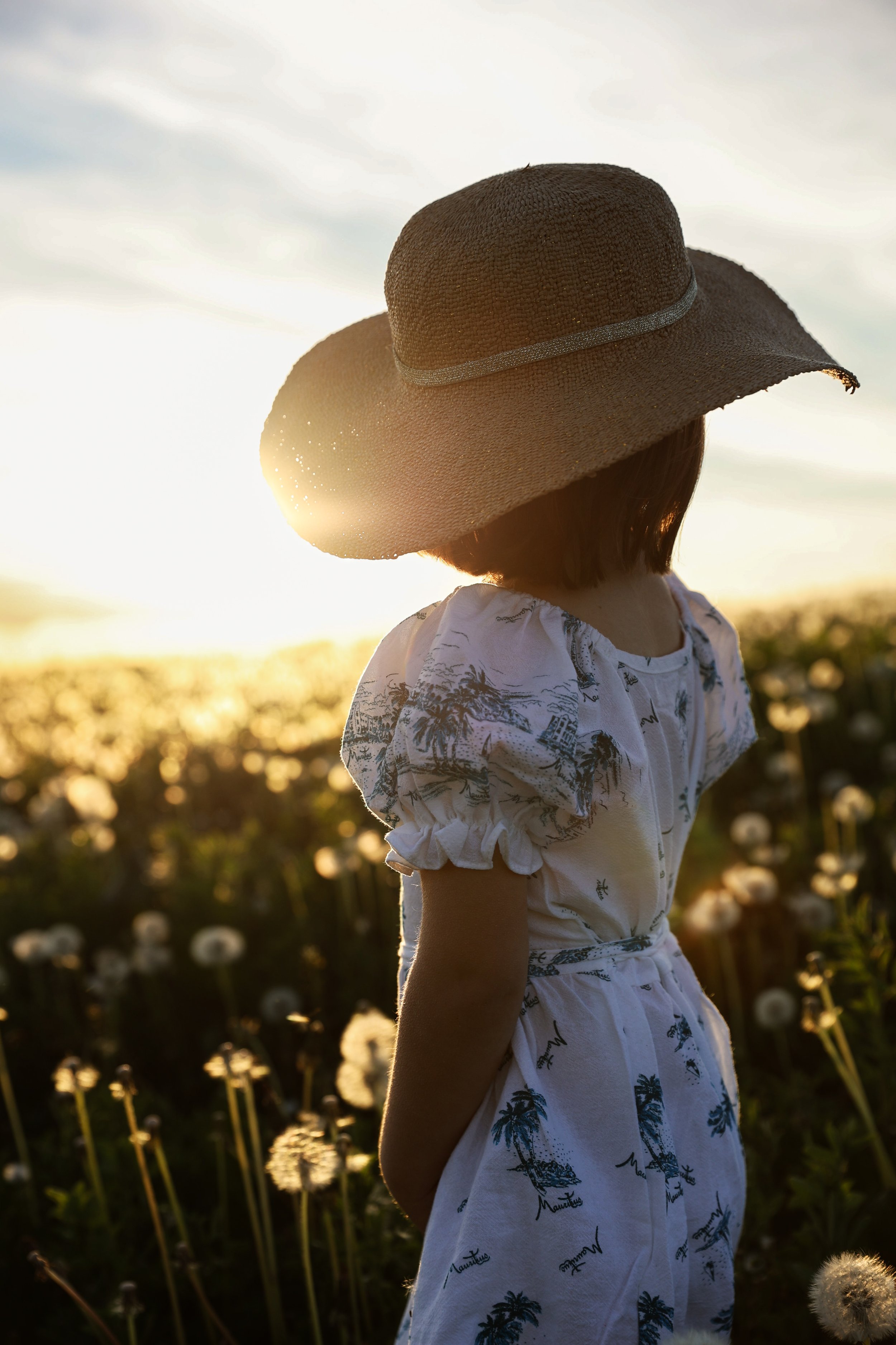 Une jeune fille portant un chapeau de paille regarde le coucher de soleil dans un champ de fleurs.
