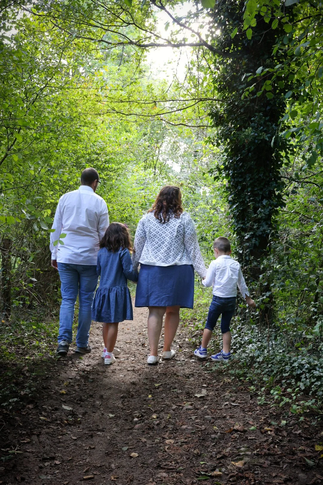 Famille marchant dans un sentier forestier verdoyant vue de derrière.