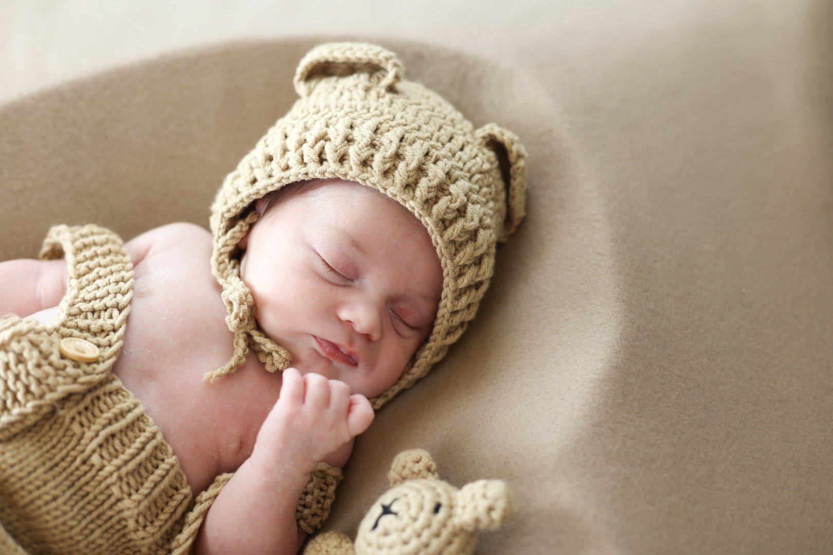 Bébé endormi portant un bonnet et un pull en laine beige, allongé sur une surface beige.