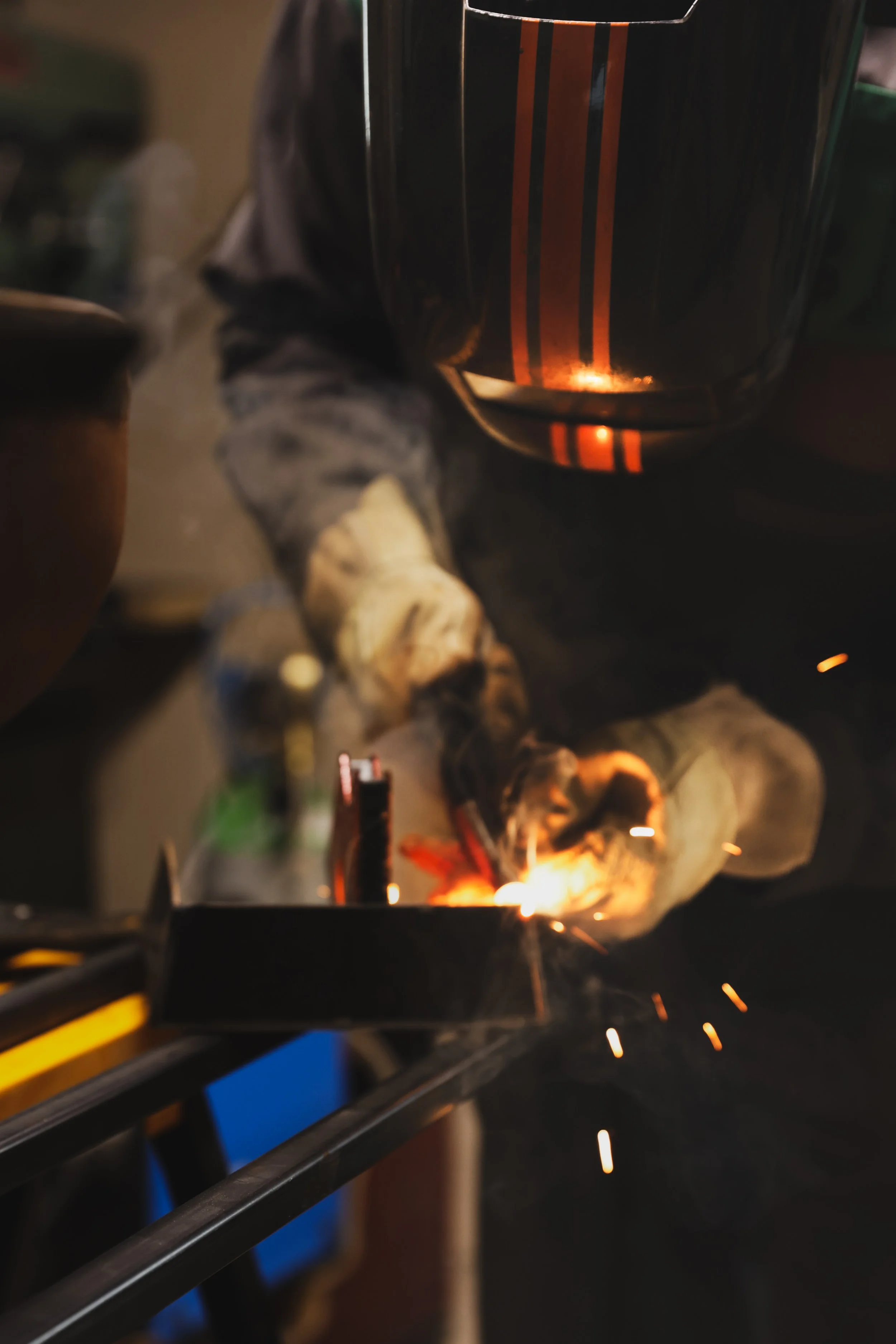 Un brasero ou une forge avec des étincelles, où un homme travaille avec un outil en train de souder ou de faire du travail du métal, entouré d'outils et d'objets en métal.