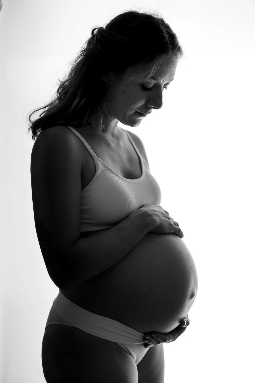 Une femme enceinte pose en regardant son ventre dans une photo en noir et blanc.