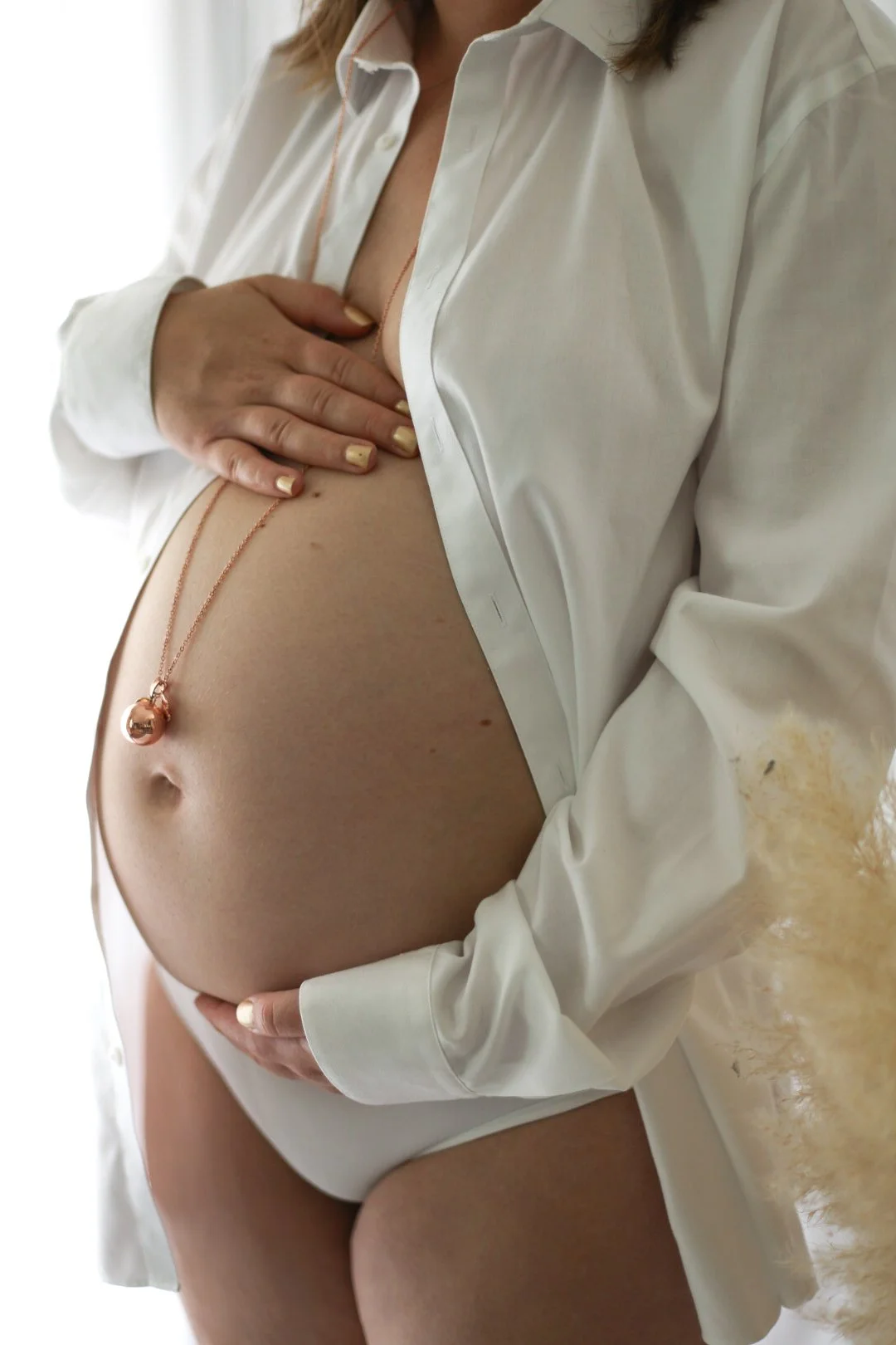 Femme enceinte portant une chemise blanche ouverte montrant son ventre.
