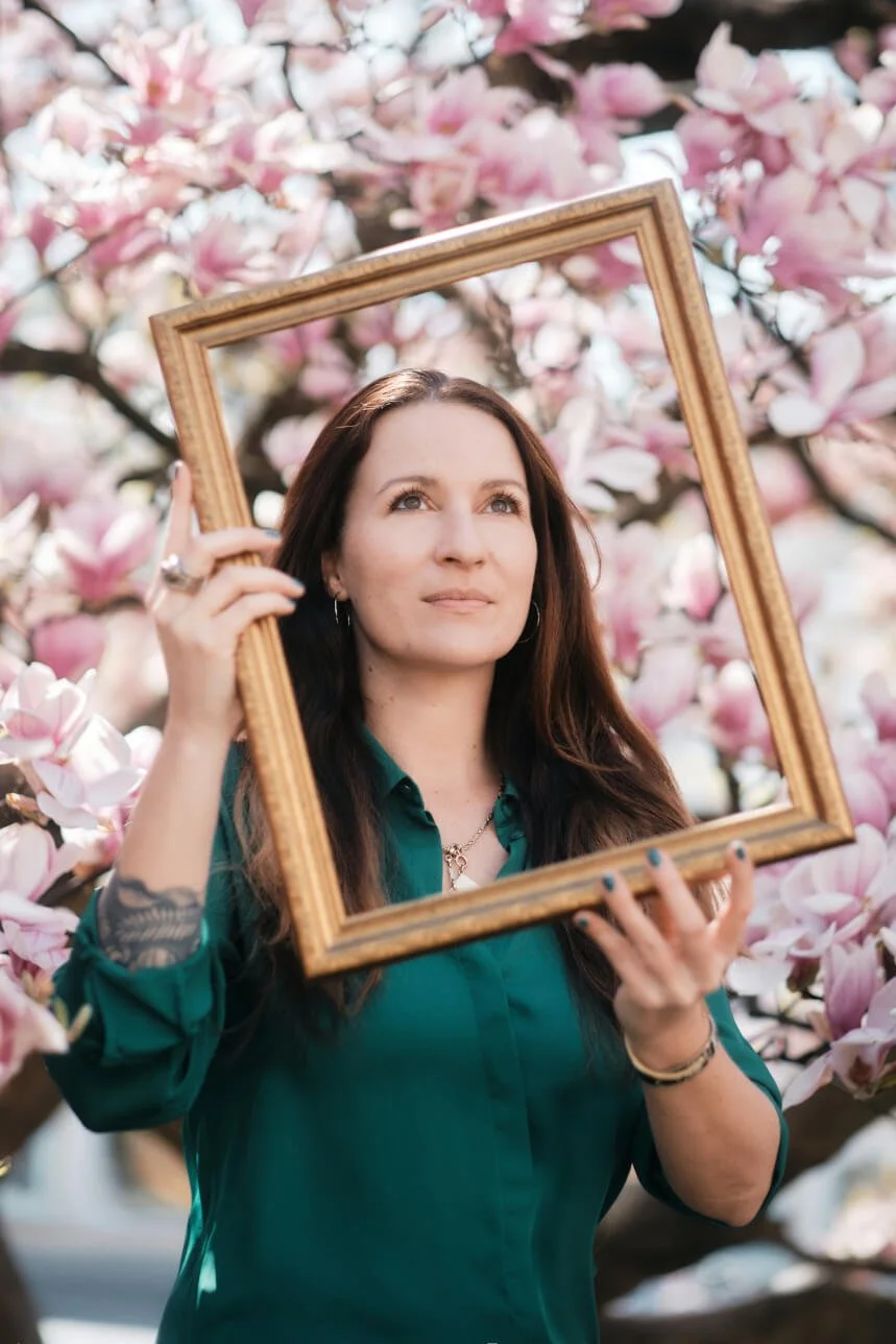 Edith Frauscher von Hummelhirn mit Bilderrahmen vor Magnolienbaum – Perspektivwechsel und Kreativität im Schreibprozess.
