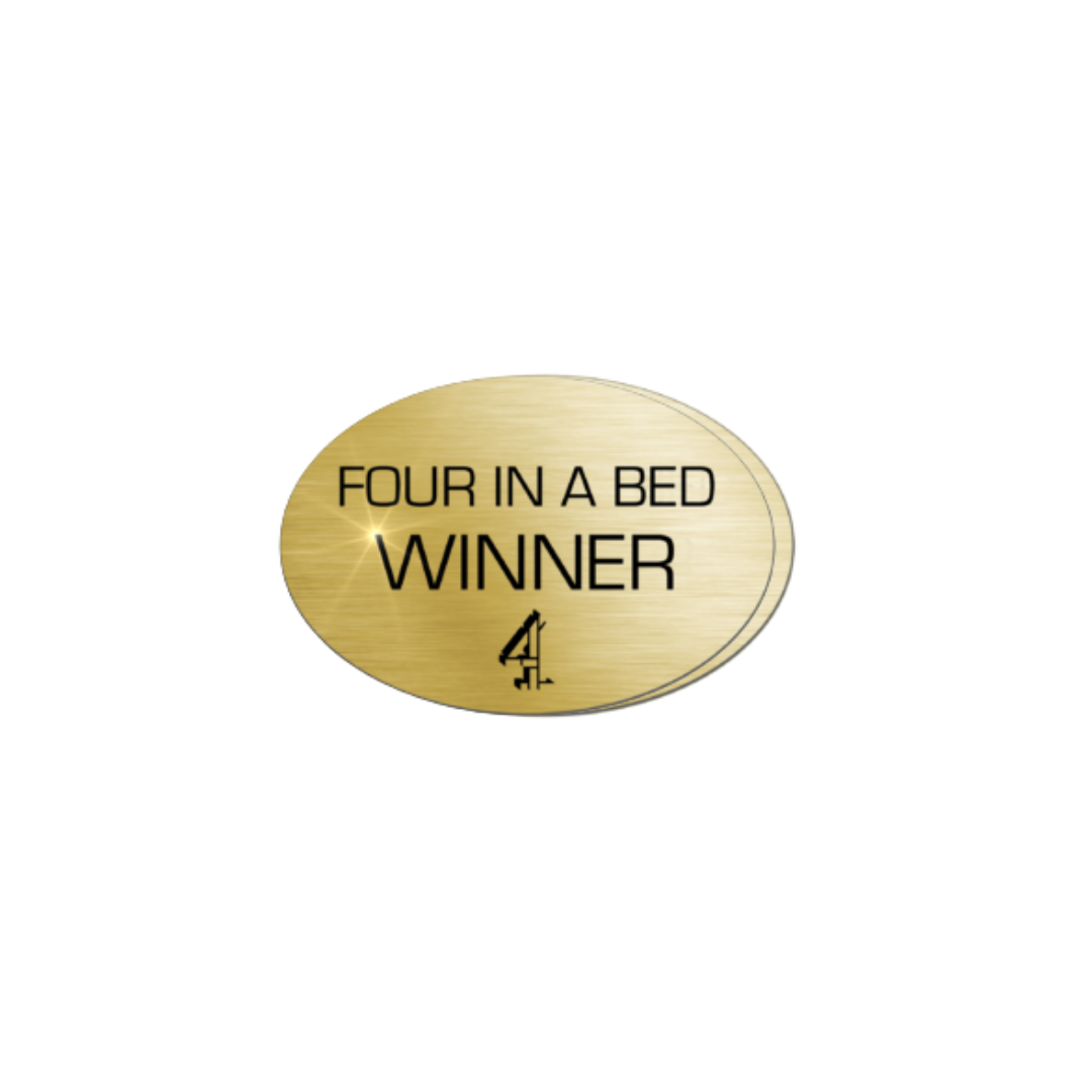 Gold oval plaque with black text that reads 'Four in a Bed Winner' and a small black logo underneath.