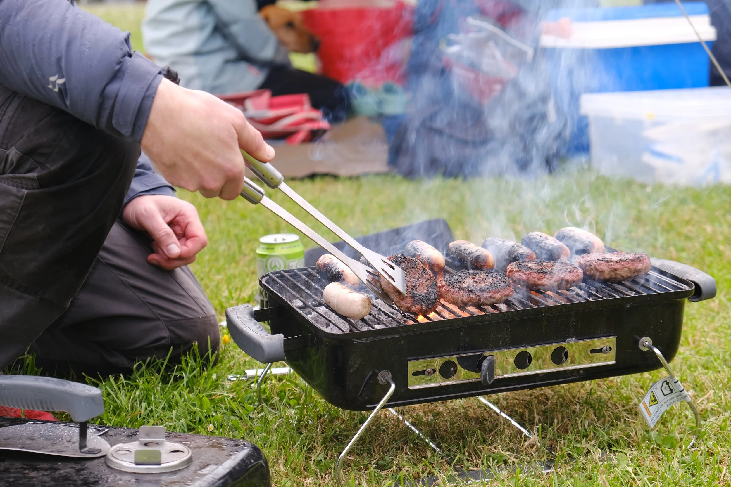 Person grilling sausages and burgers on an outdoor barbecue grill.