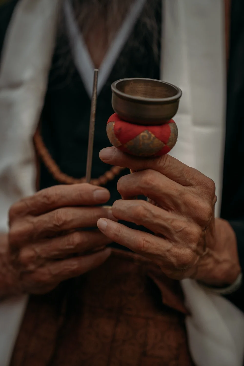 Nahaufnahme einer älteren Person, die eine kleine, handgefertigte Schale auf einer bunten, traditionellen Socke hält und eine Gebetskette trägt.