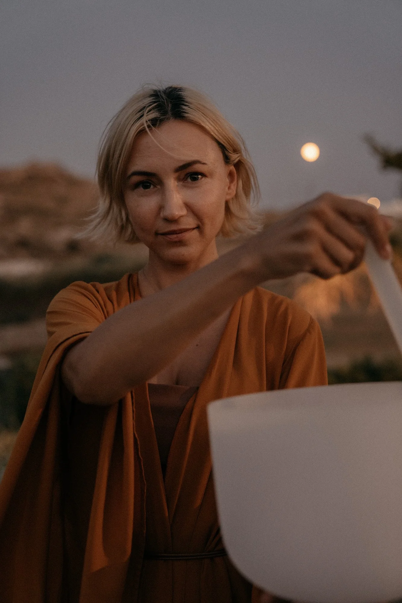 Frau mit kurzen blonden Haaren, die auf einer Terrasse bei Sonnenuntergang Bier einschenkt.