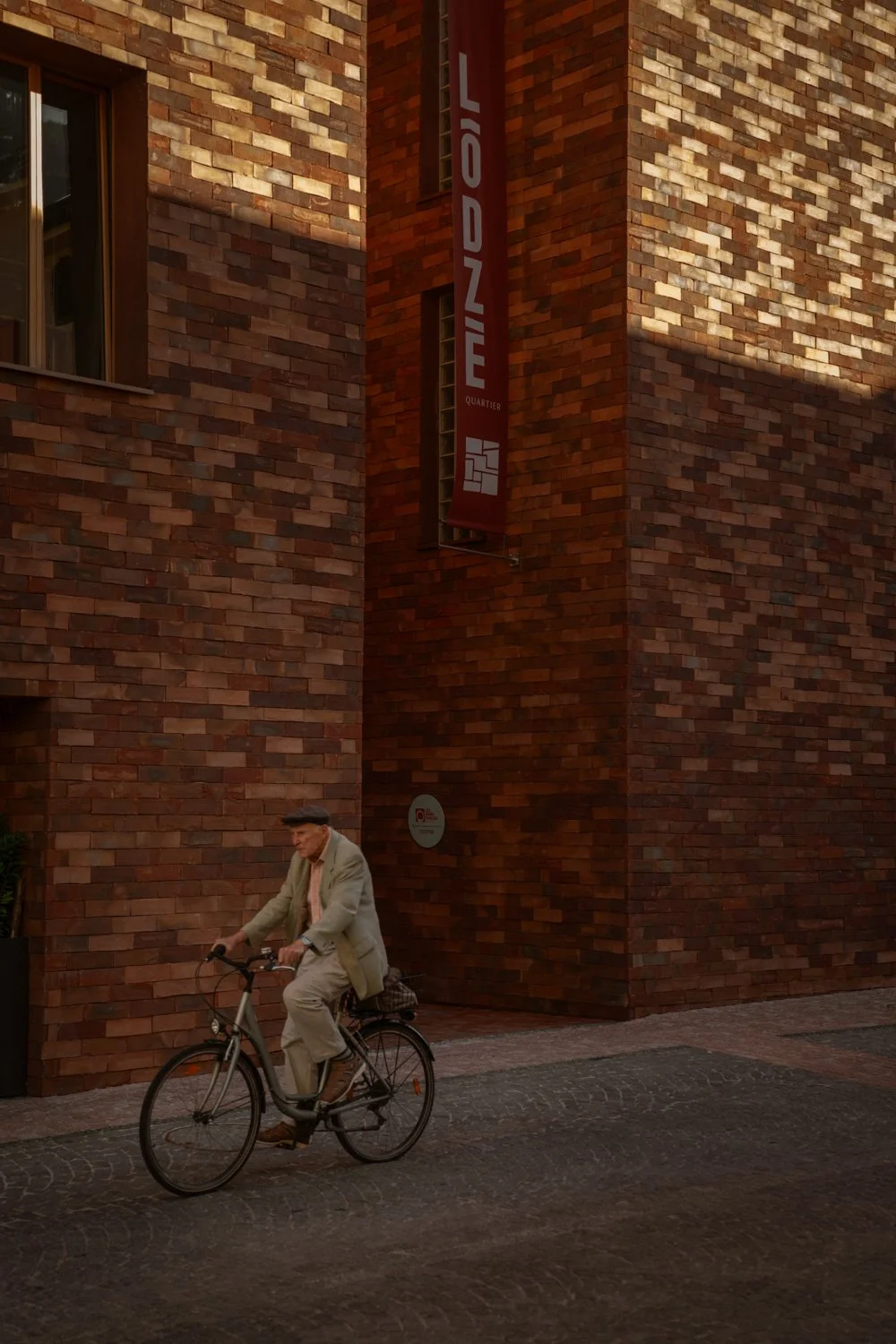Älterer Mann in grauem Anzug fährt Fahrrad an einer roten Backsteinwand.
