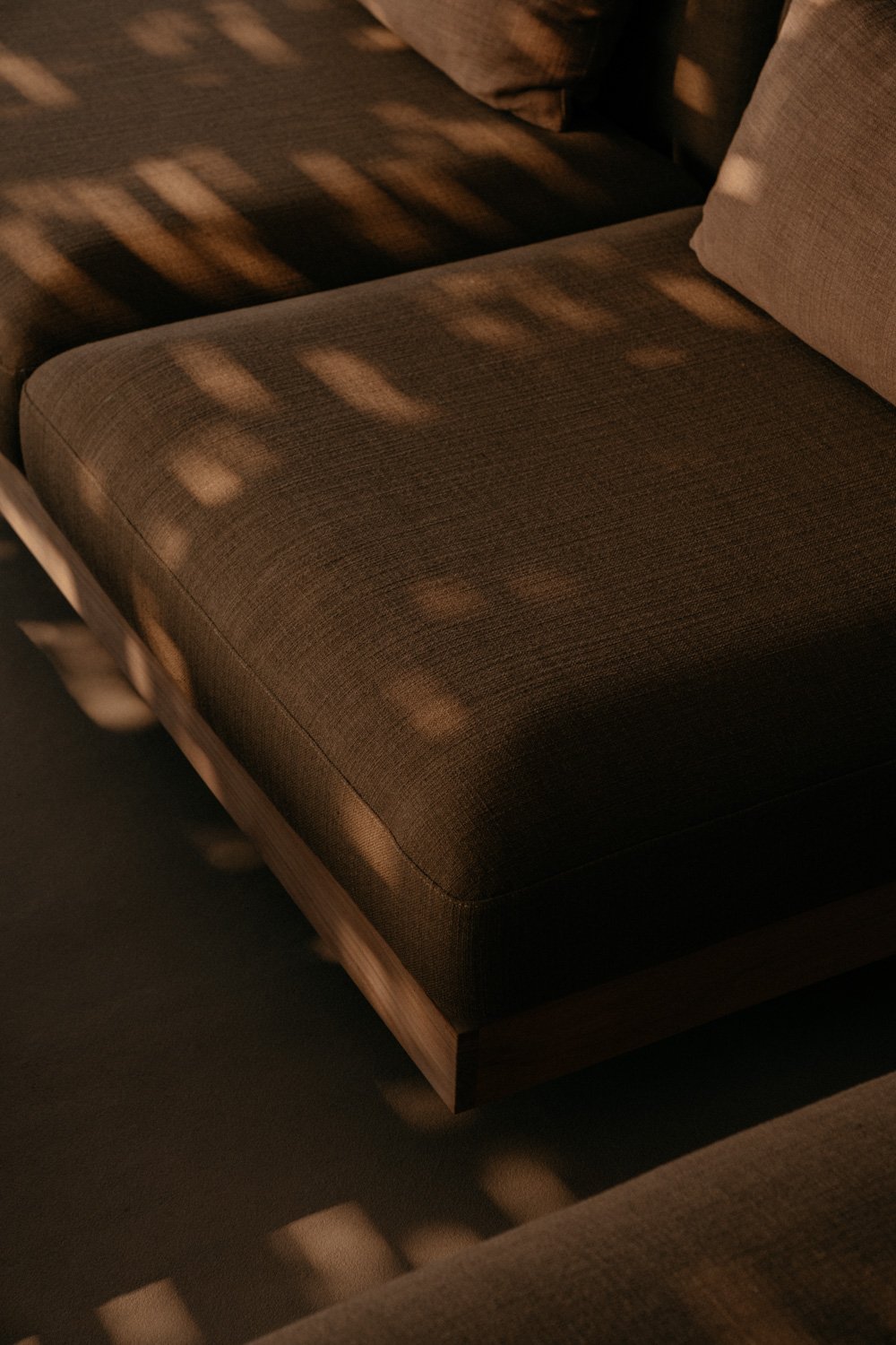 Ein braunes Sofakissen mit Lichtern, die durch Fenster auf das Sofa fallen.