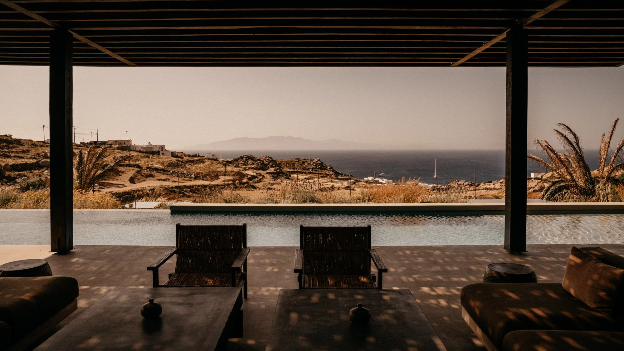 Blick von einer offenen Terrasse mit Blick auf das Meer, Hügel und einige Gebäude in einer ländlichen Gegend.