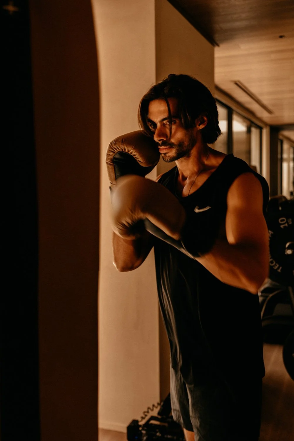 Mann trainiert mit Boxhandschuhen in einem Fitnessstudio, trainiert gegen eine Wand, dunkler Raum, fokussierte Stimmung.
