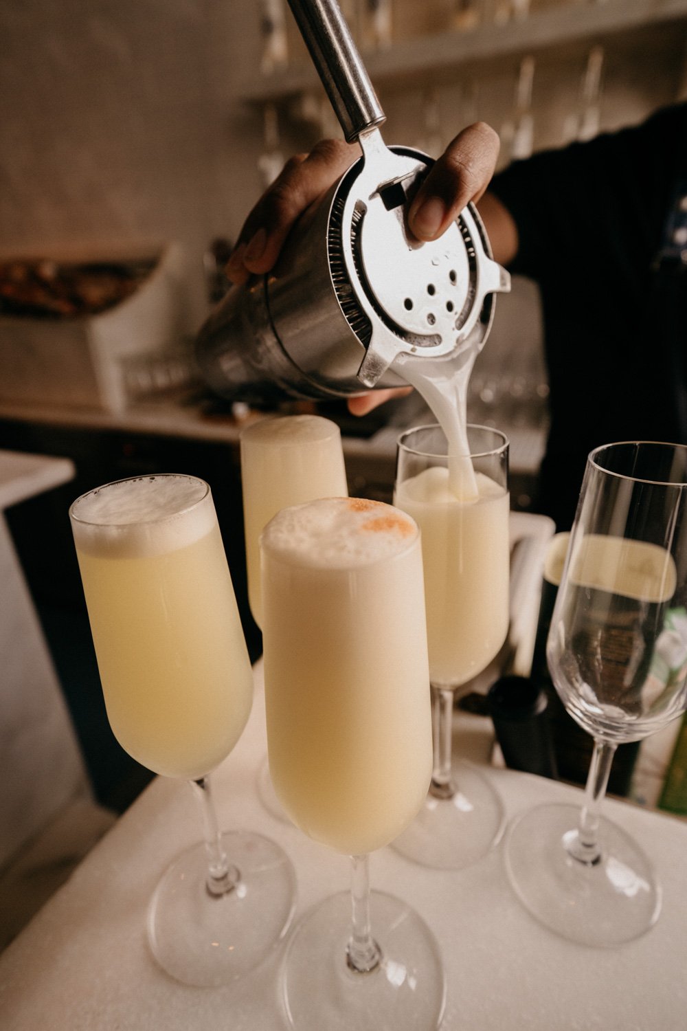 Person gießt Champagner in Sektgläser, während andere Gläser auf einem Tisch stehen.