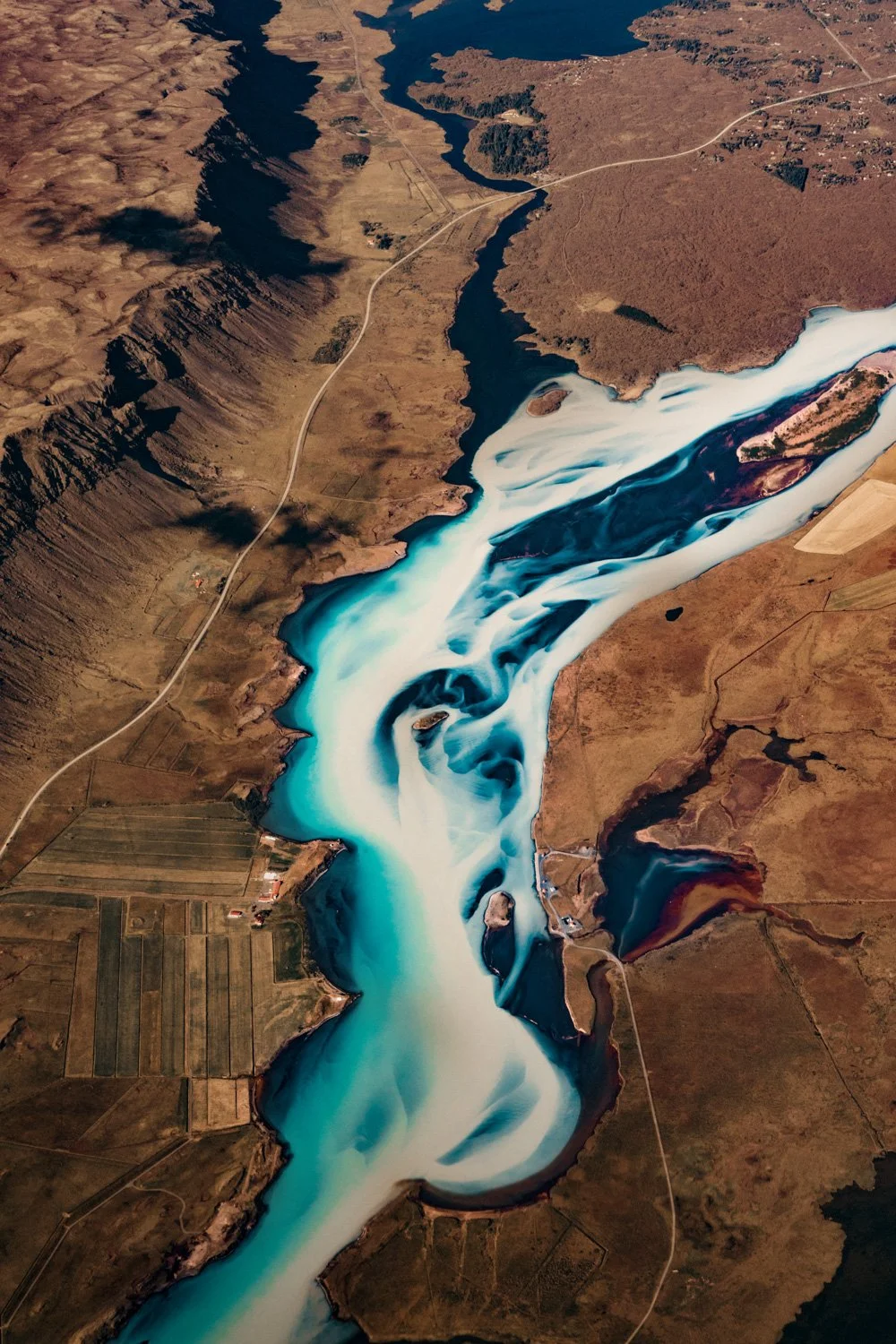 Eine Seenlandschaft mit tiefblauem Wasser, das von braunen, felsigen und bewaldeten Hängen umgeben ist. Es gibt eine Straße, die sich durch die Landschaft zieht.