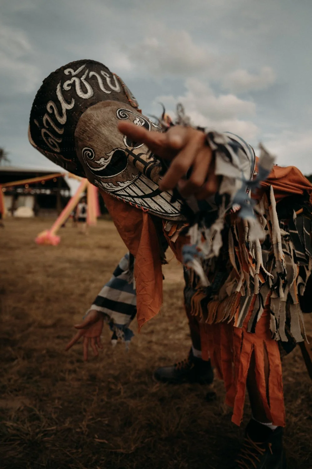 Person in farbenfroher traditioneller Kleidung und Hut, die eine Pose macht, bei einem outdoor Festival oder Event bei Sonnenuntergang.