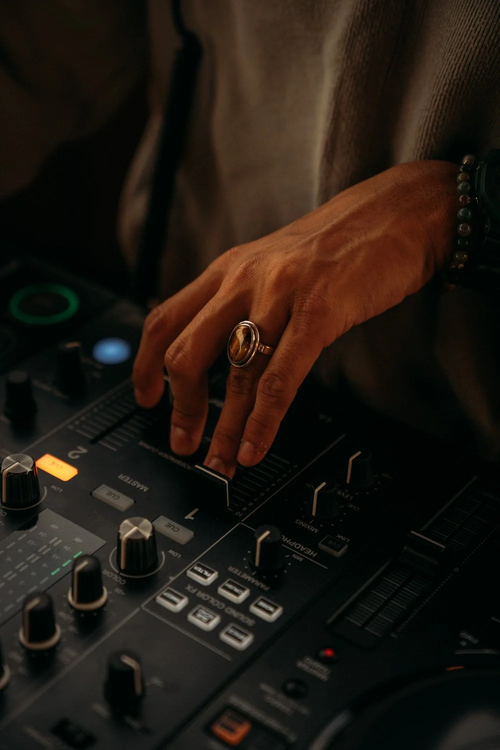 Hände eines DJs, der einen Mixer bedient, mit einem Ring und Armband, dunkle Beleuchtung.