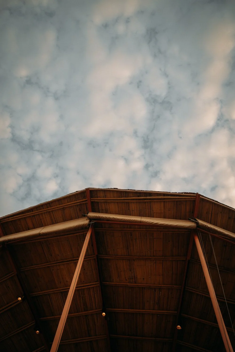 Blick nach oben auf die Holzdecke eines Pavillons bei Bewölktem Himmel.