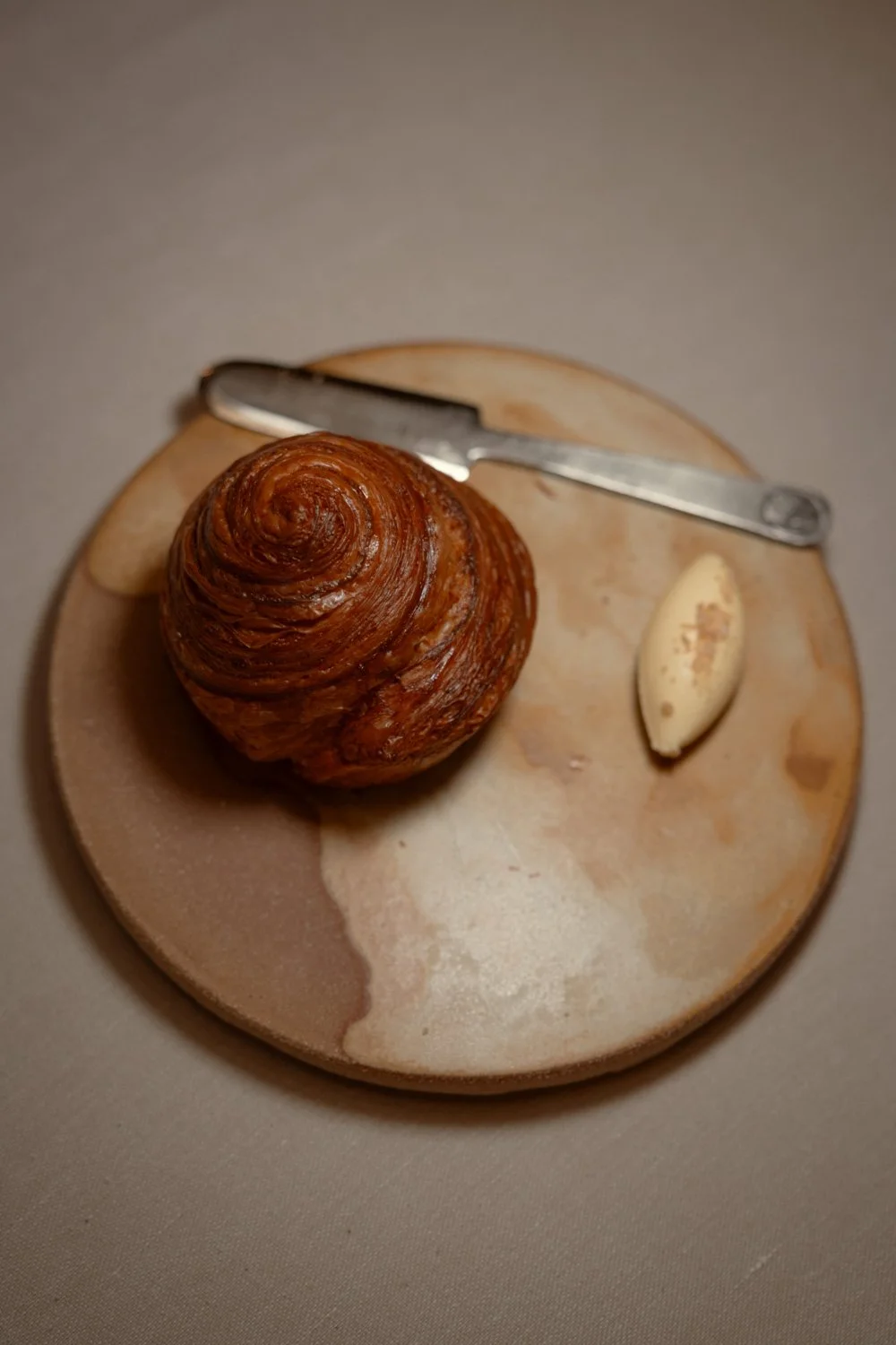 Ein Croissant auf einem runden Steinuntersetzer, daneben ein Messer und eine Knoblauchknolle.