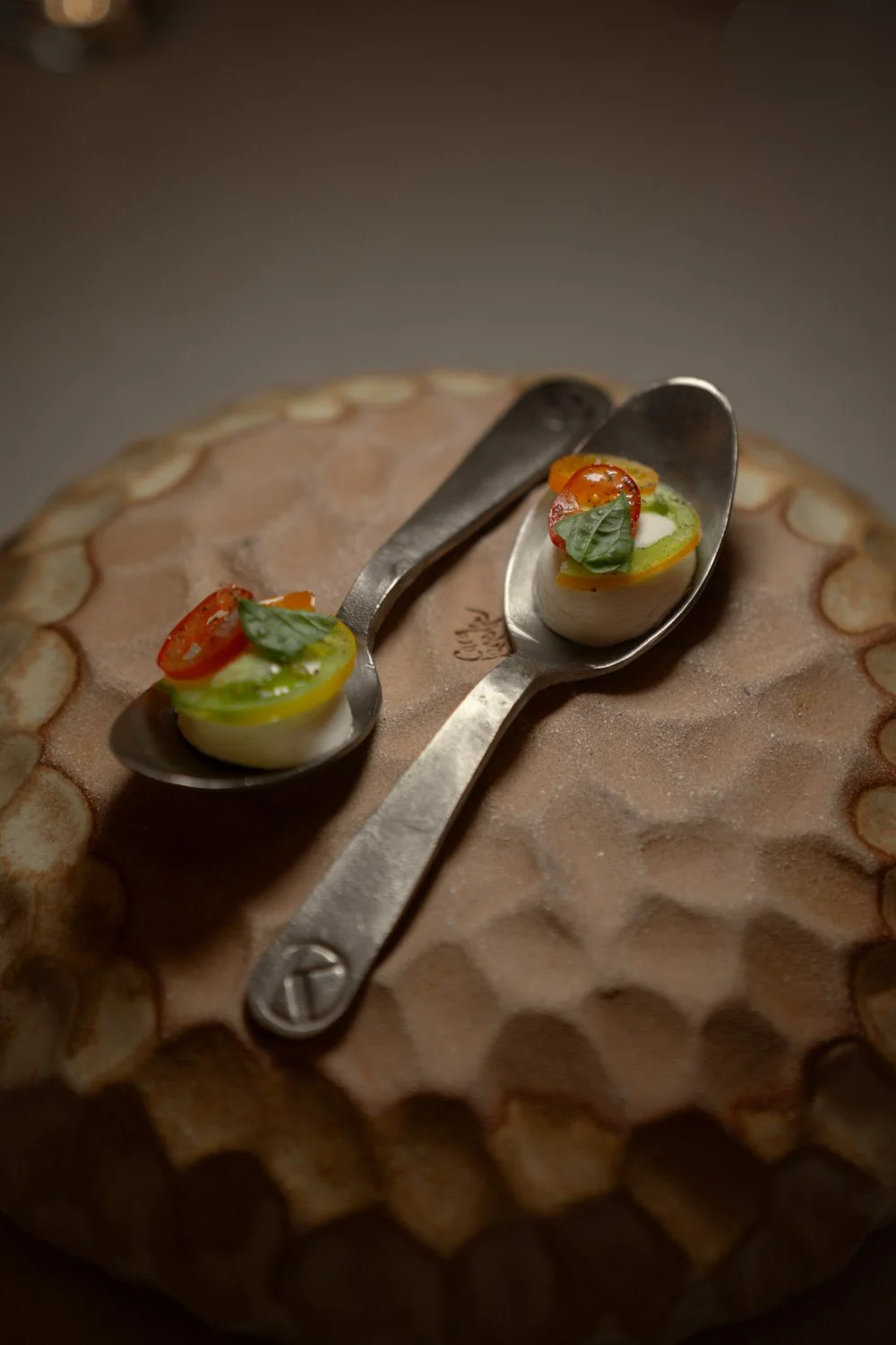 Käse mit roten und grünen Tomaten und Basilikum, serviert auf Löffeln, auf einem Käseblock