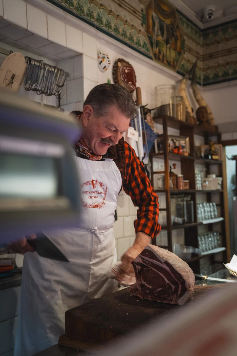 Ein Mann schneidet ein großes Stück rohes Fleisch auf einer Holzplatte in einer Küche.