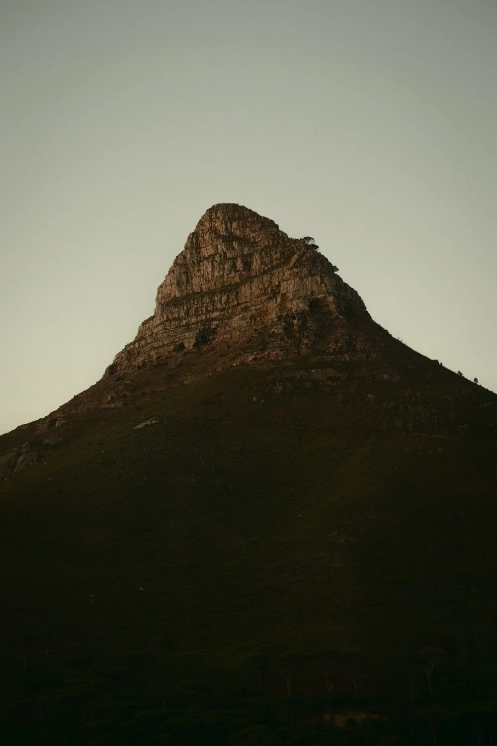 Berg mit steiler, felsiger Spitze und dunklem Abhang, bei Sonnenuntergang