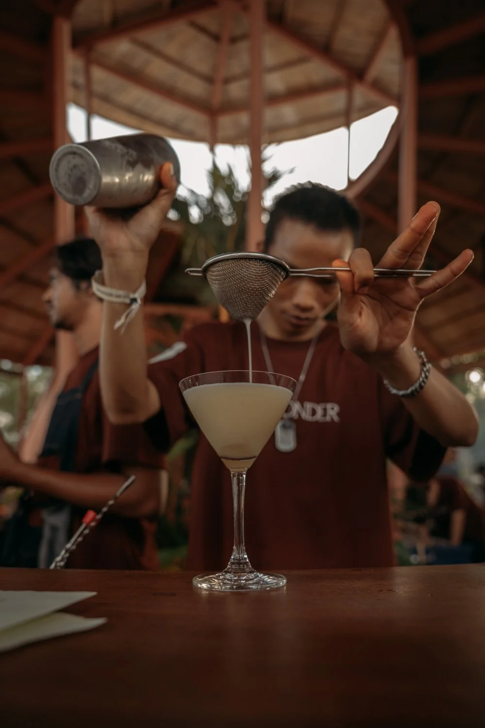 Junger Mann filmt einen Cocktail in einem Bar-Glas, während ein anderer im Hintergrund steht.