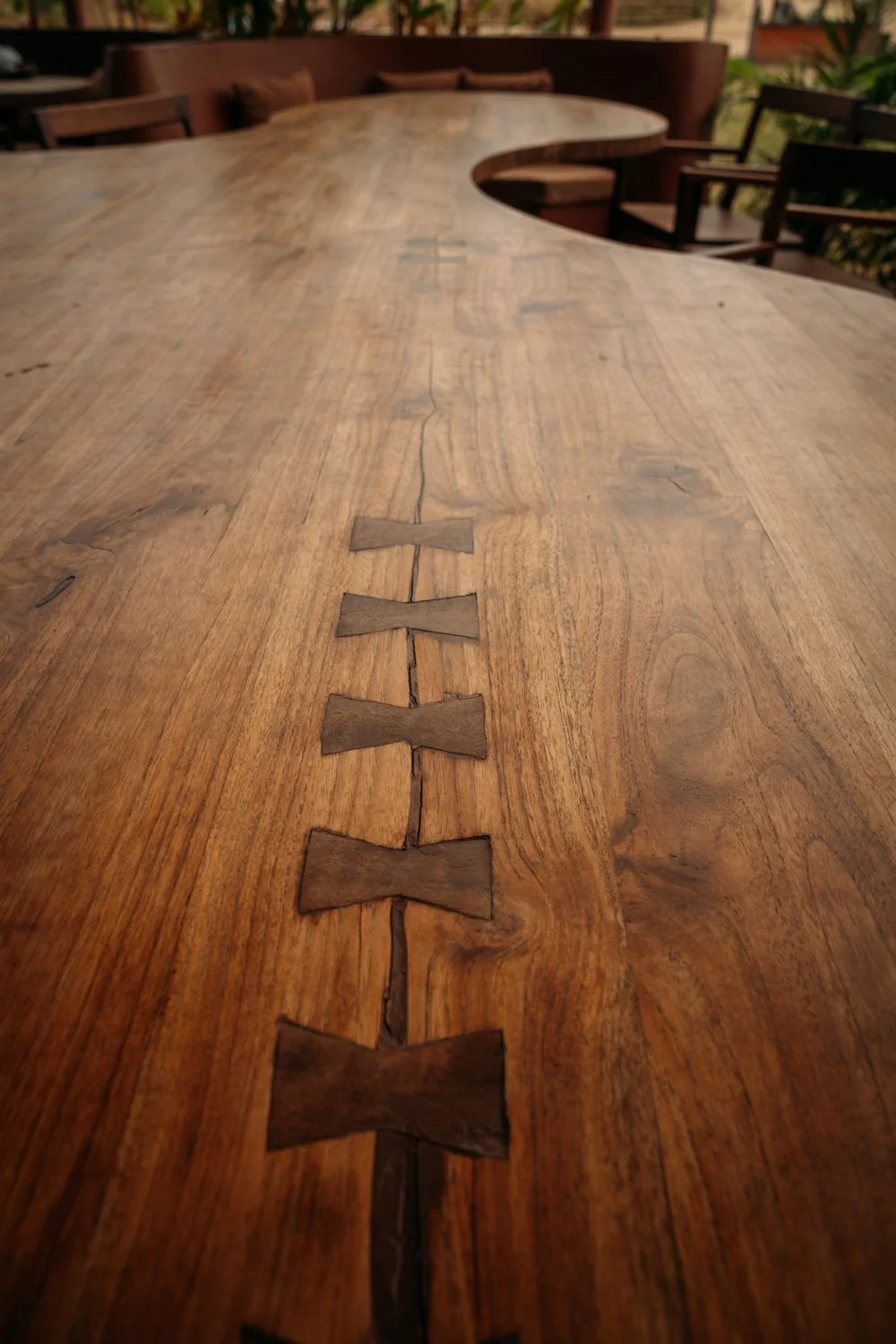 Langer holztisch mit inlay aus dunkleren Holzstücken, auf einer Terrasse mit Garten im Hintergrund.