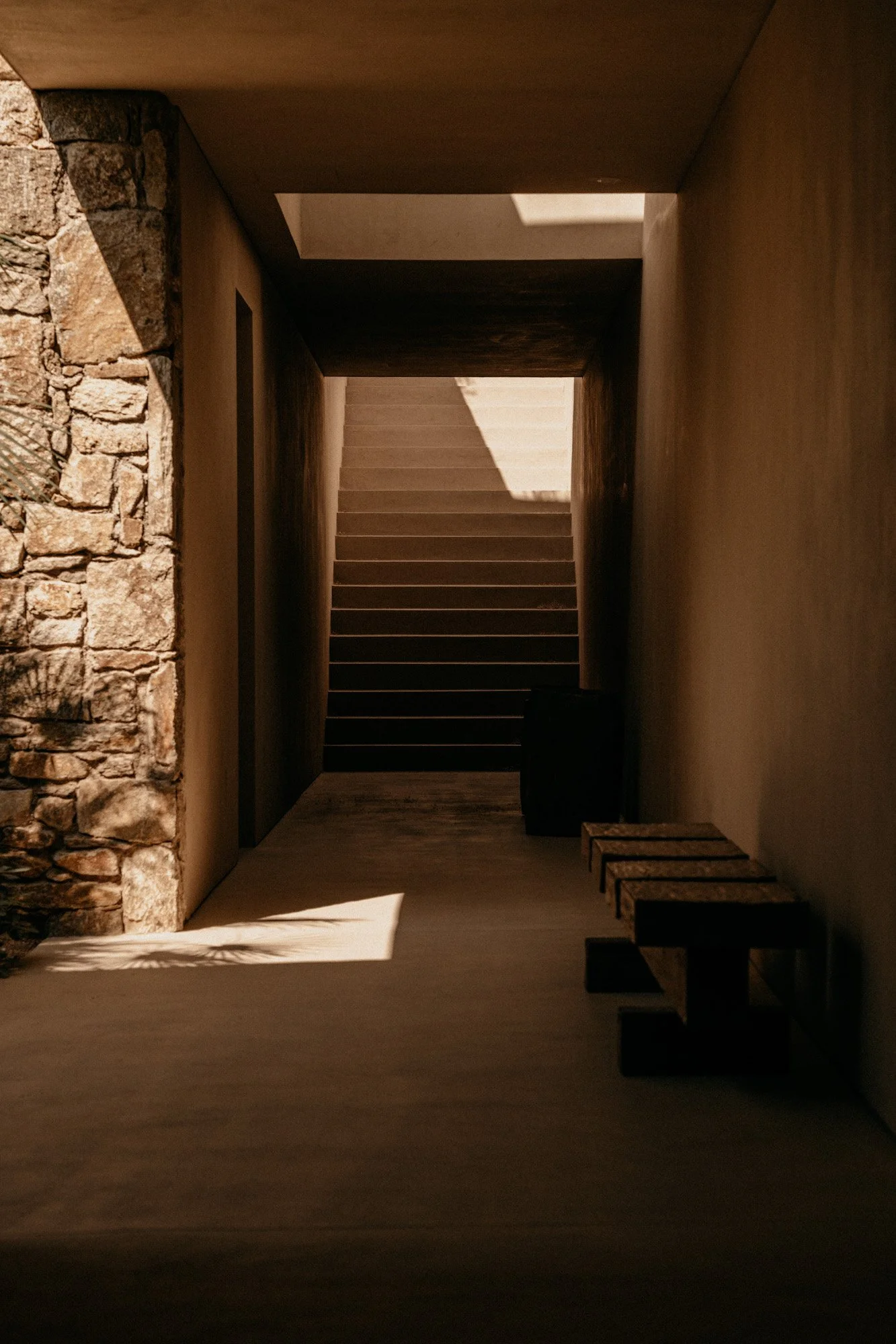 Ein moderner Innenraum mit Steinstützmauern, Treppe und Sonnenlicht, das einen Schatten an die Wand wirft.