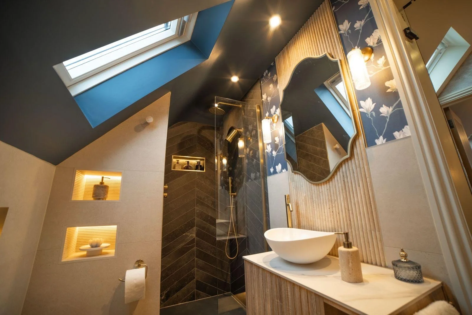 Modern bathroom with skylight, dark and beige tile walls, gold fixtures, decorative mirror, and a vessel sink on a wooden vanity.