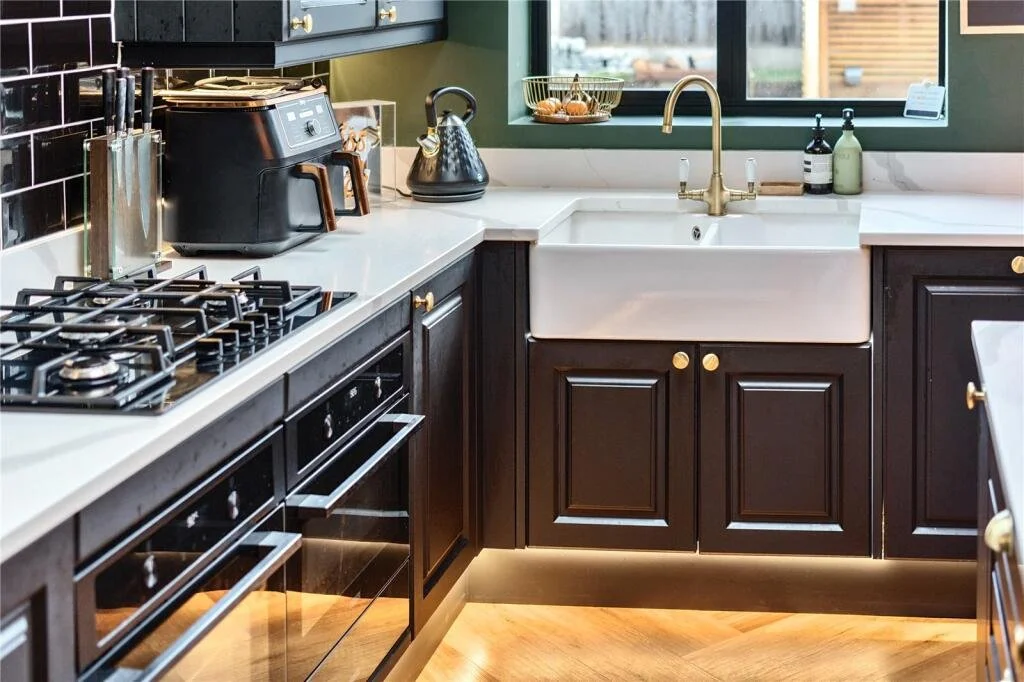 Kitchen with black cabinets, white countertop, sink, window, black stove, toaster, kettle, and countertop containers.