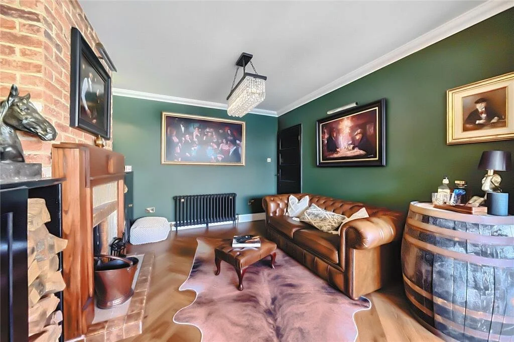 Living room with green walls, a leather sofa, framed paintings, a fireplace, a wooden barrel bar, a cowhide rug, and various decorative items.
