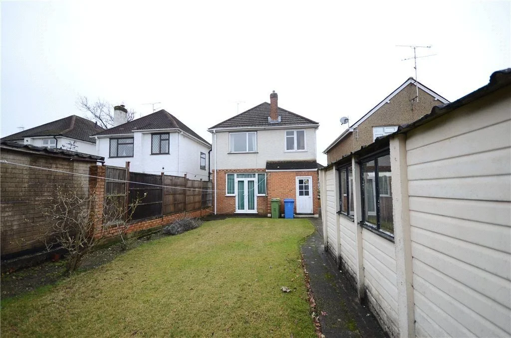 Backyard with a grassy lawn, a small tree, and a shed on the right. Several houses with chimneys and antennae are visible in the background.