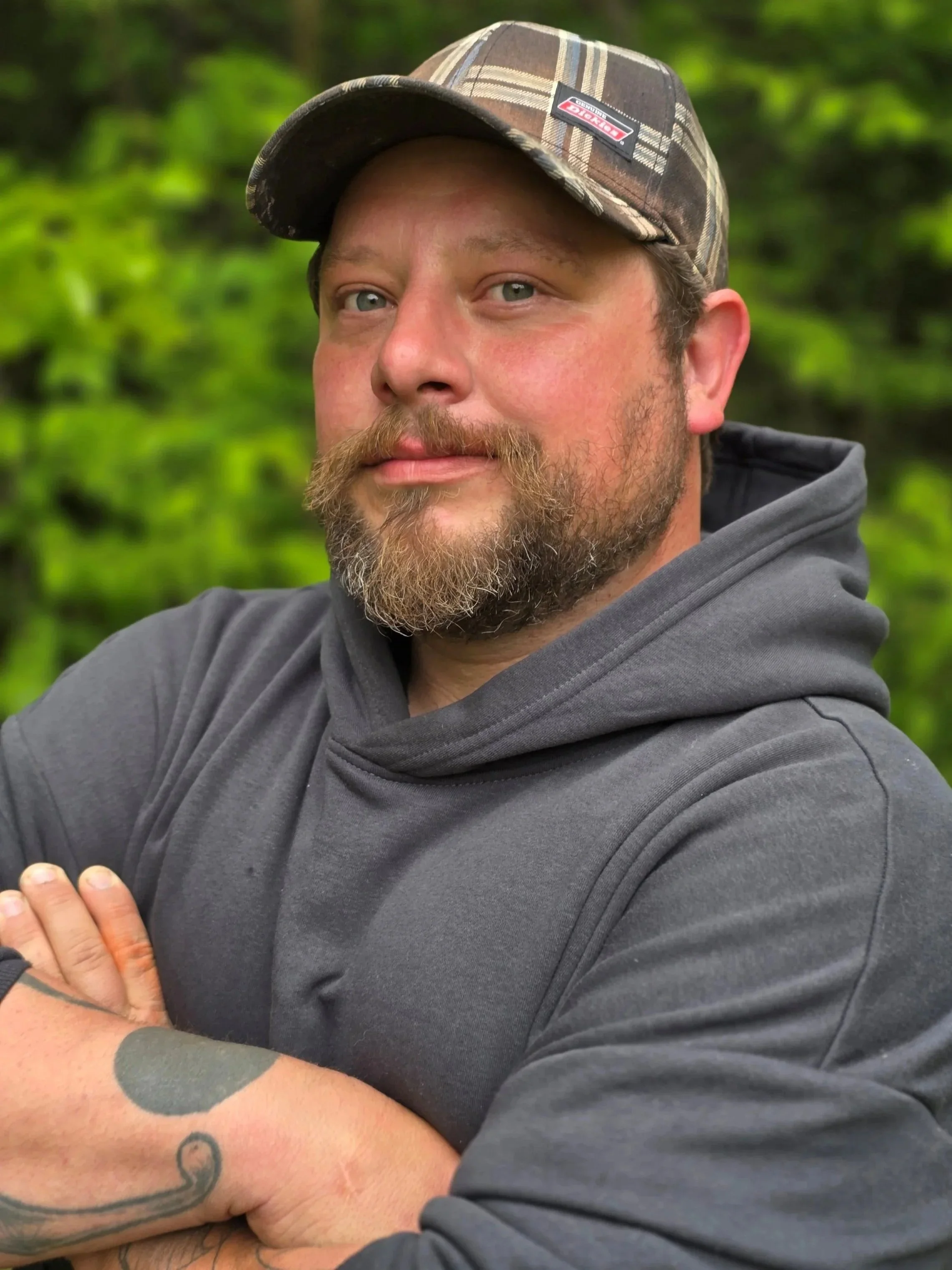 A man with a beard and mustache wearing a plaid cap and a gray hoodie.