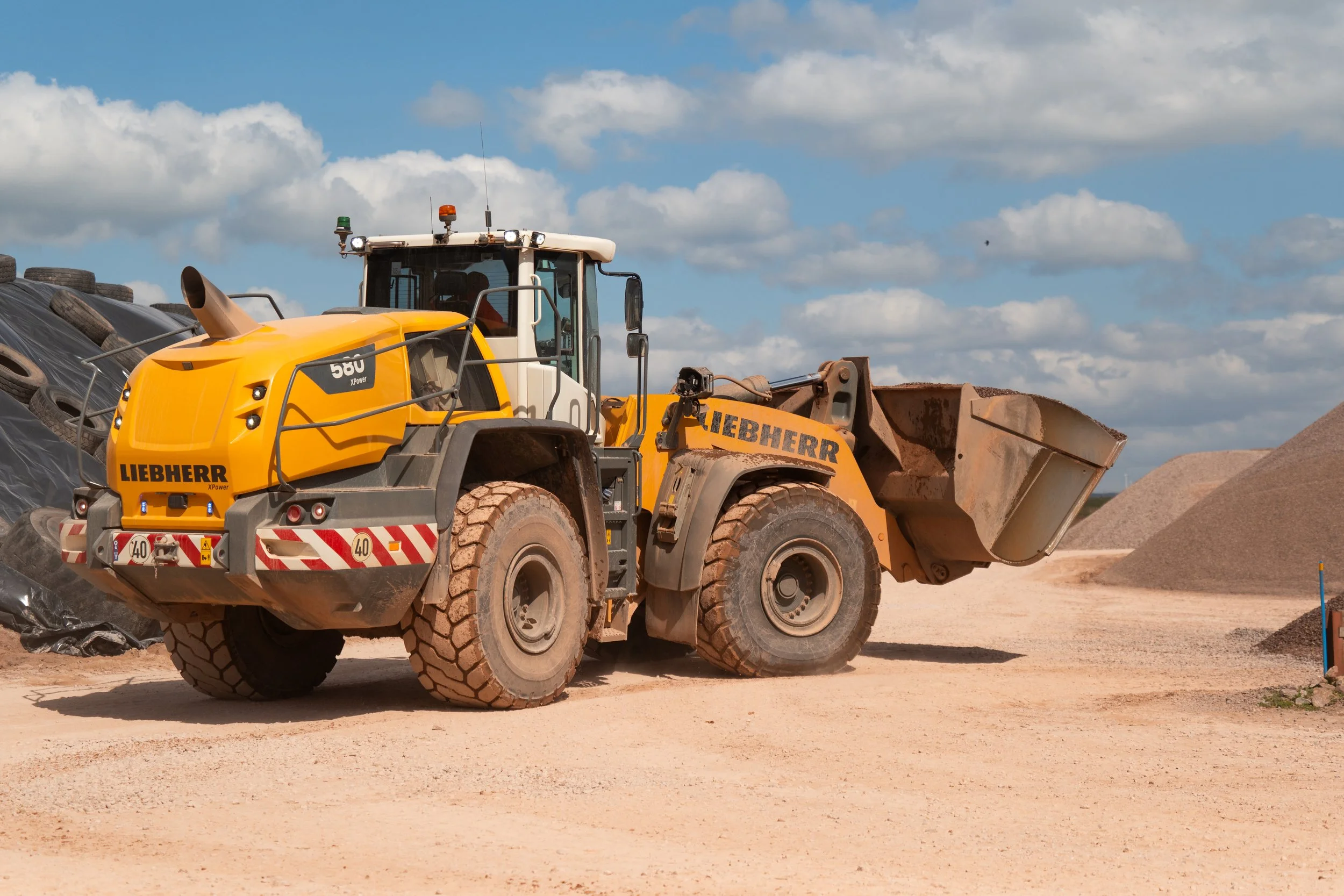 A yellow Liebherr wheel loader with dirt on its tires, operating on a construction site under a partly cloudy sky.